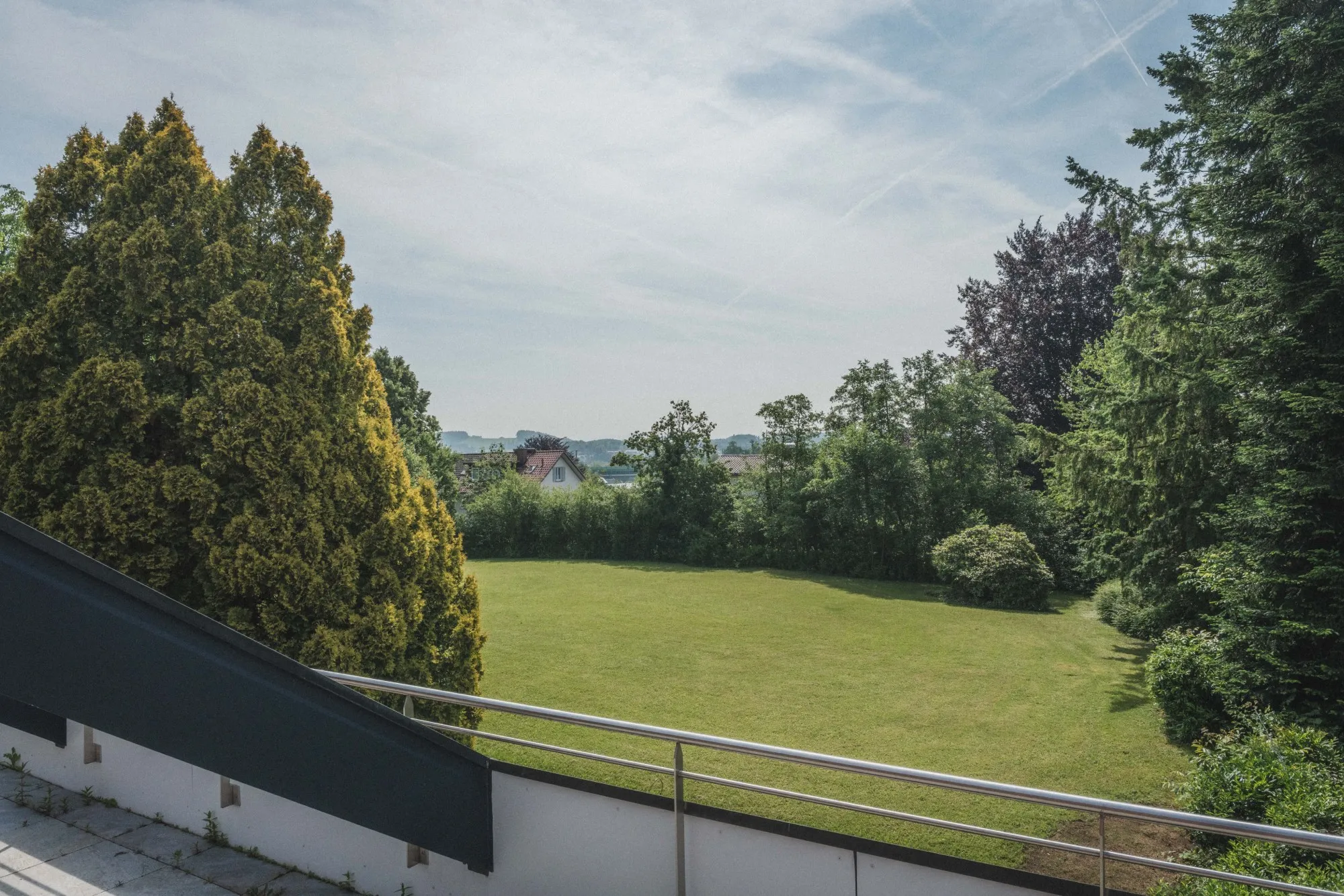 Ausblick von einem Balkon ins Grüne mit Bäumen und Wiese.