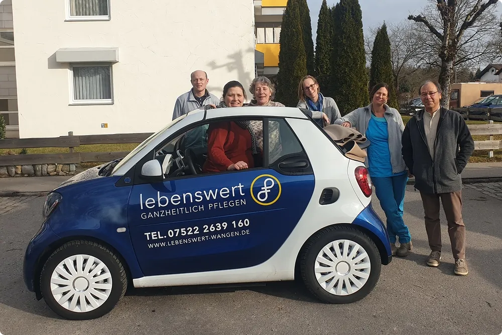 Mehrere Mitarbeiter von lebenswert Wangen posieren vor einem Geschäftsauto des Pflegedienstes.