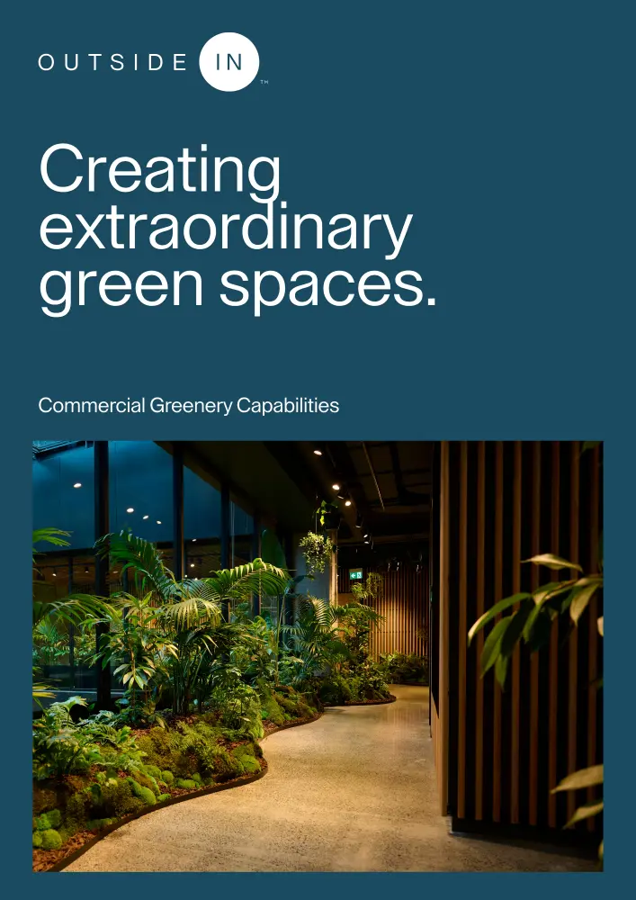 Dark teal background with the white text 'OUTSIDE IN Creating extraordinary green spaces. Commercial Greenery Capabilities' above a photo of an indoor garden with lush green plants along a curved path inside a modern building with wooden paneling and glass windows.