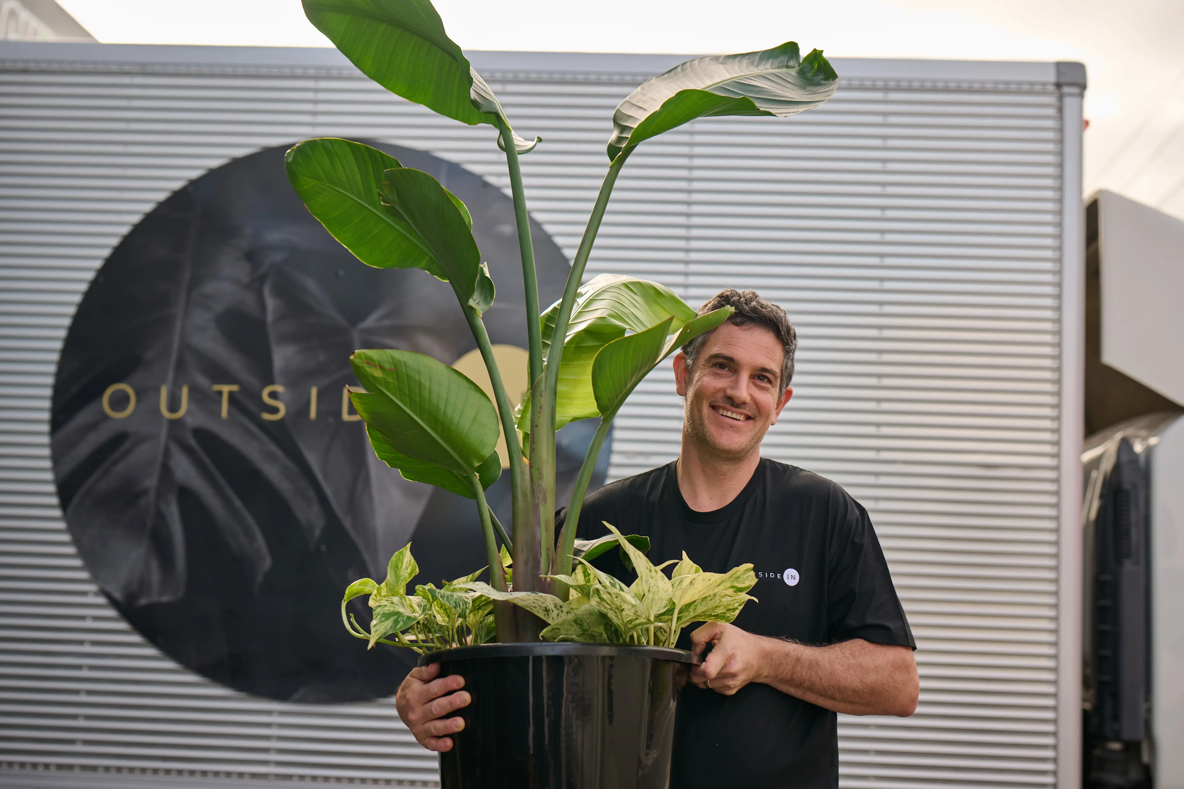 Outside In employee holding plant pot in front of Outside In logo.