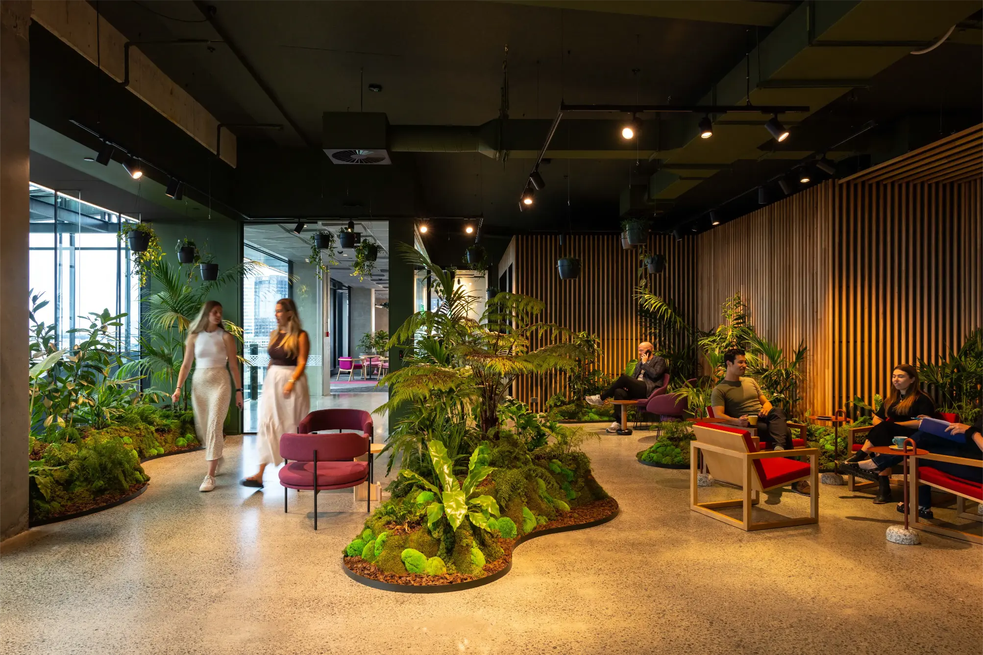 Side-by-side image showing a modern open-plan cafeteria before and after adding large white planters filled with lush green plants, brightening the space and adding natural décor near tables and seating areas.