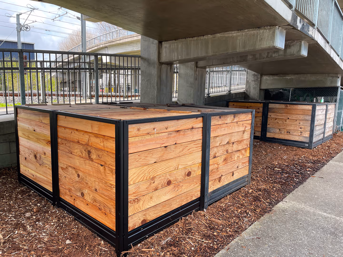 Custom timber and steel raised planter boxes installed under an overpass structure as part of a commercial urban sustainability design project