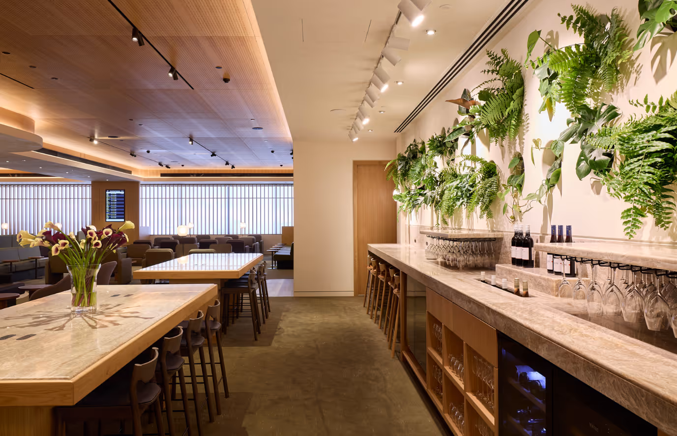 Dining and lounge area in the Qantas International Business Lounge at Auckland Airport, featuring a green feature wall with layered foliage, warm timber joinery, and soft seating