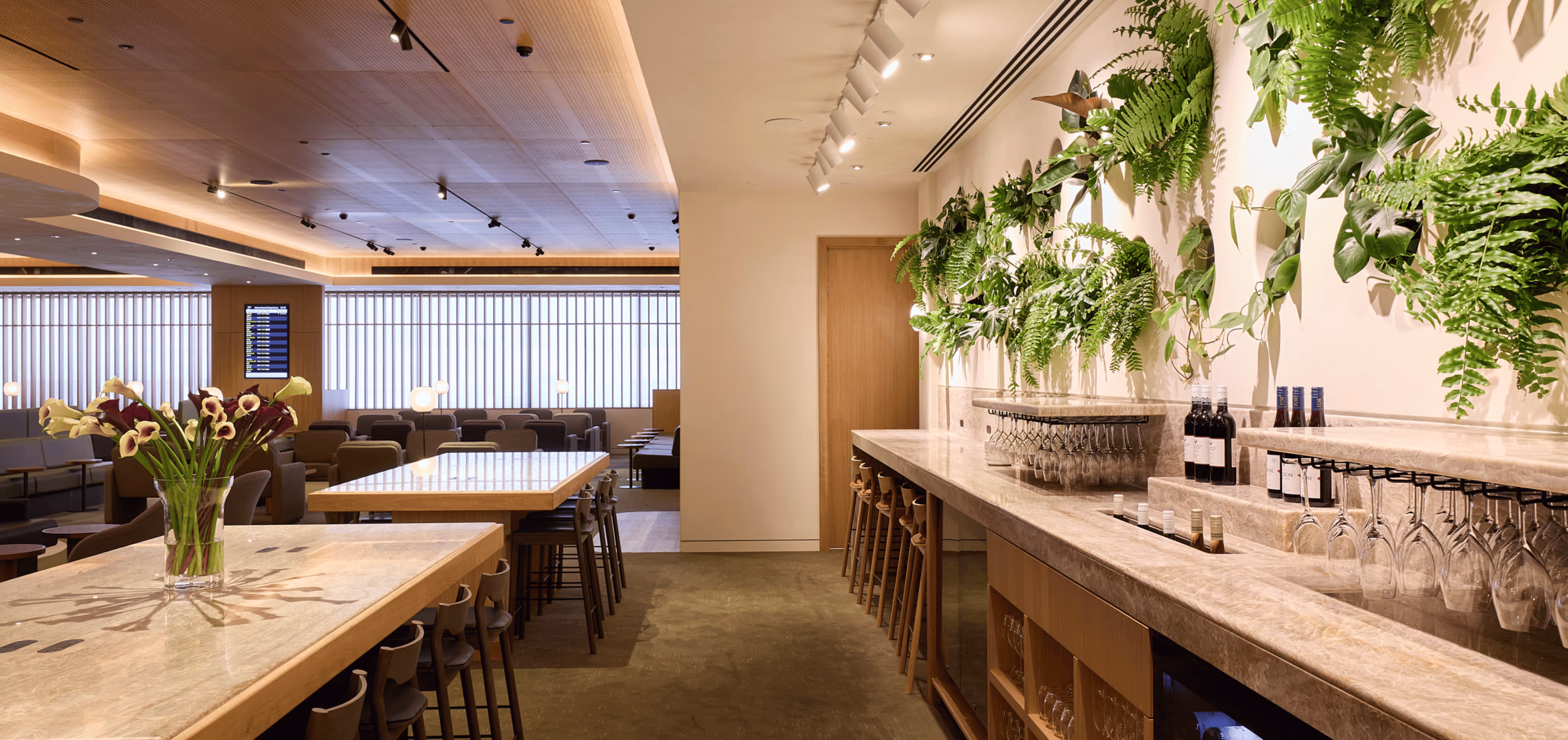 Dining and lounge area in the Qantas International Business Lounge at Auckland Airport, featuring a green feature wall with layered foliage, warm timber joinery, and soft seating