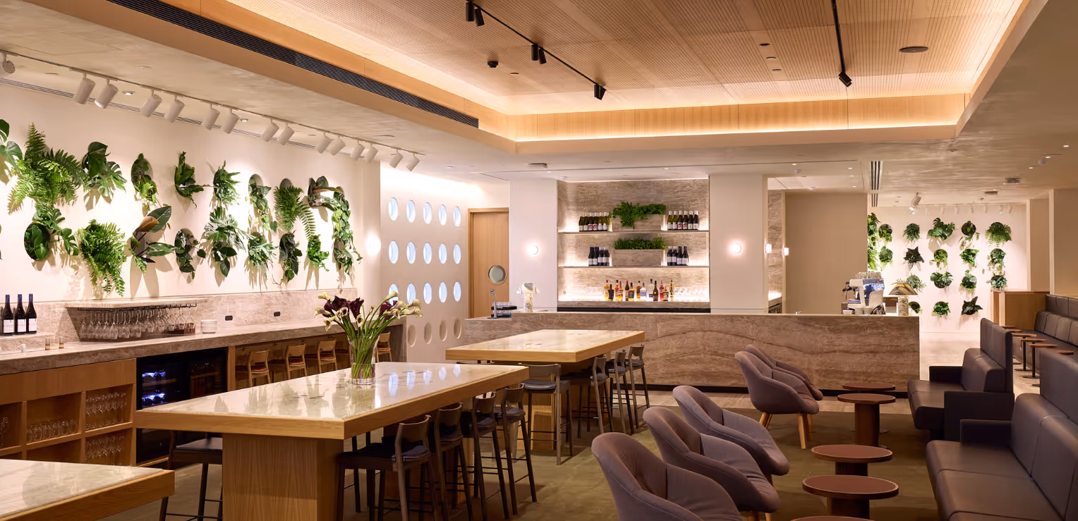 Dining and lounge area in the Qantas International Business Lounge at Auckland Airport, featuring a green feature wall with layered foliage, warm timber joinery, and soft seating