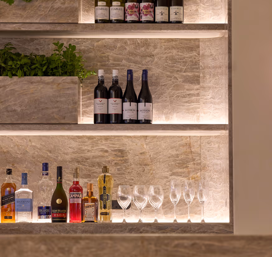 Bar shelving in the Qantas International Business Lounge at Auckland Airport, styled with curated greenery, wine bottles, and glassware against a textured stone backdrop