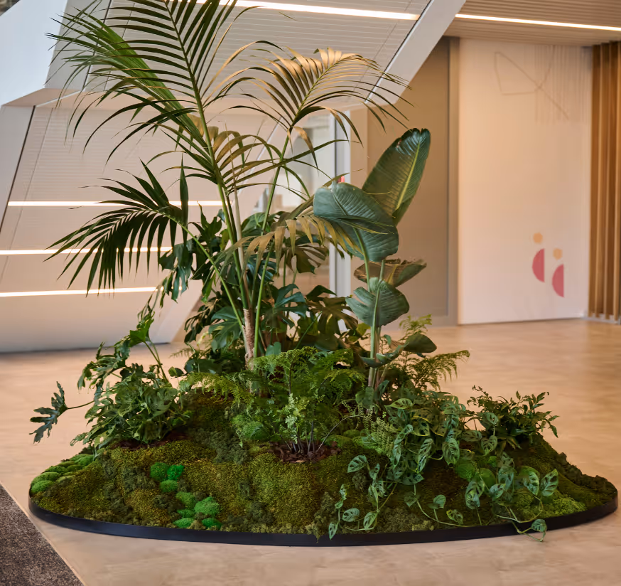 Forest-form sculptural planter beneath a stairwell at Deloitte Auckland with layered tropical palms, ferns and moss, creating a lush focal point in a bright open-plan corridor