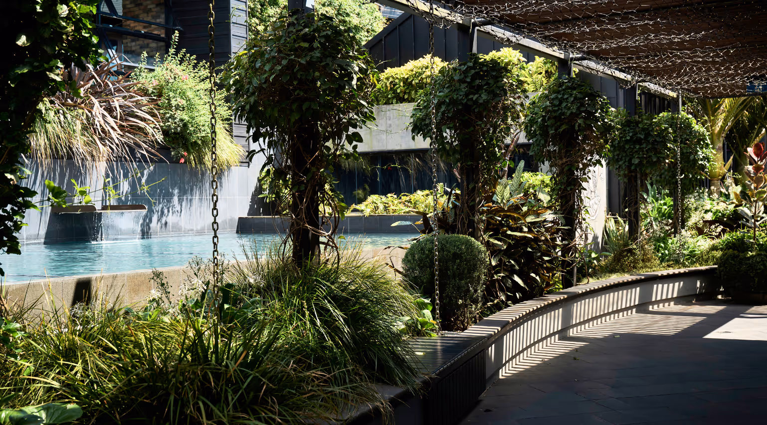 Lush bespoke exterior planting scheme with layered greenery, water feature and climbing plants designed by Outside In for a commercial outdoor precinct