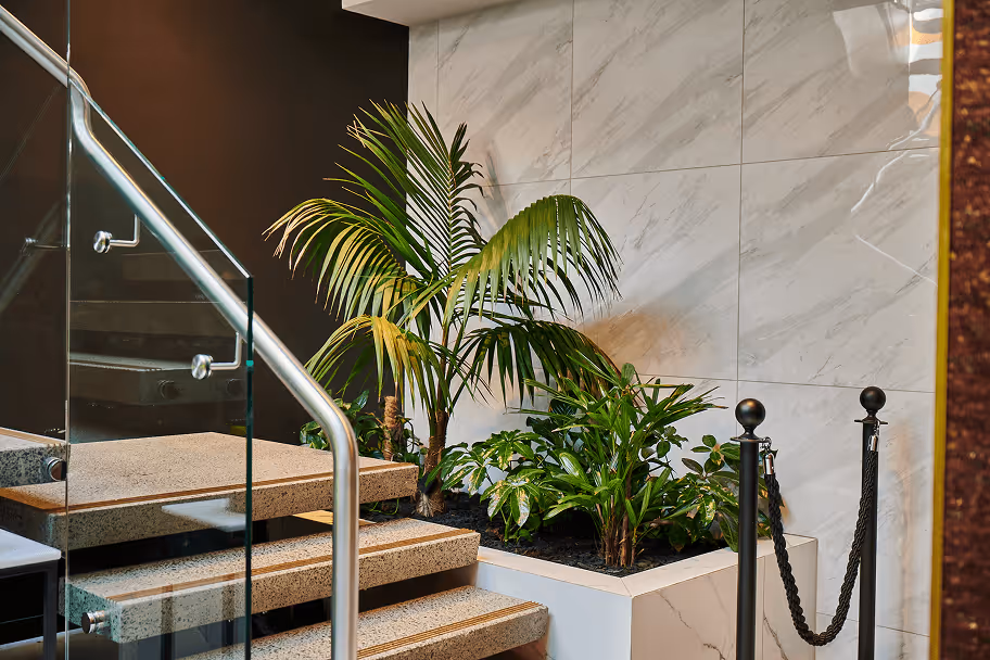 Hotel staircase landing with a planted garden bed featuring palms and tropical ferns, softening the transitional space and enhancing the overall guest experience