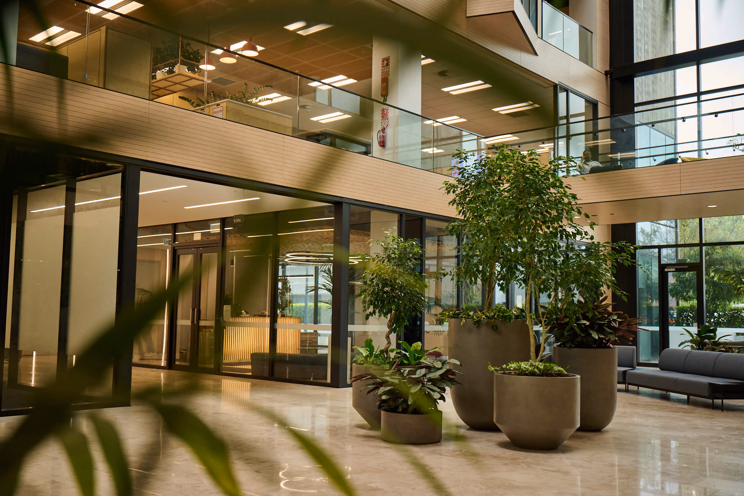 The two-storey Broadway atrium — taupe planters of ficus trees and tropical foliage, with glass offices on both levels.