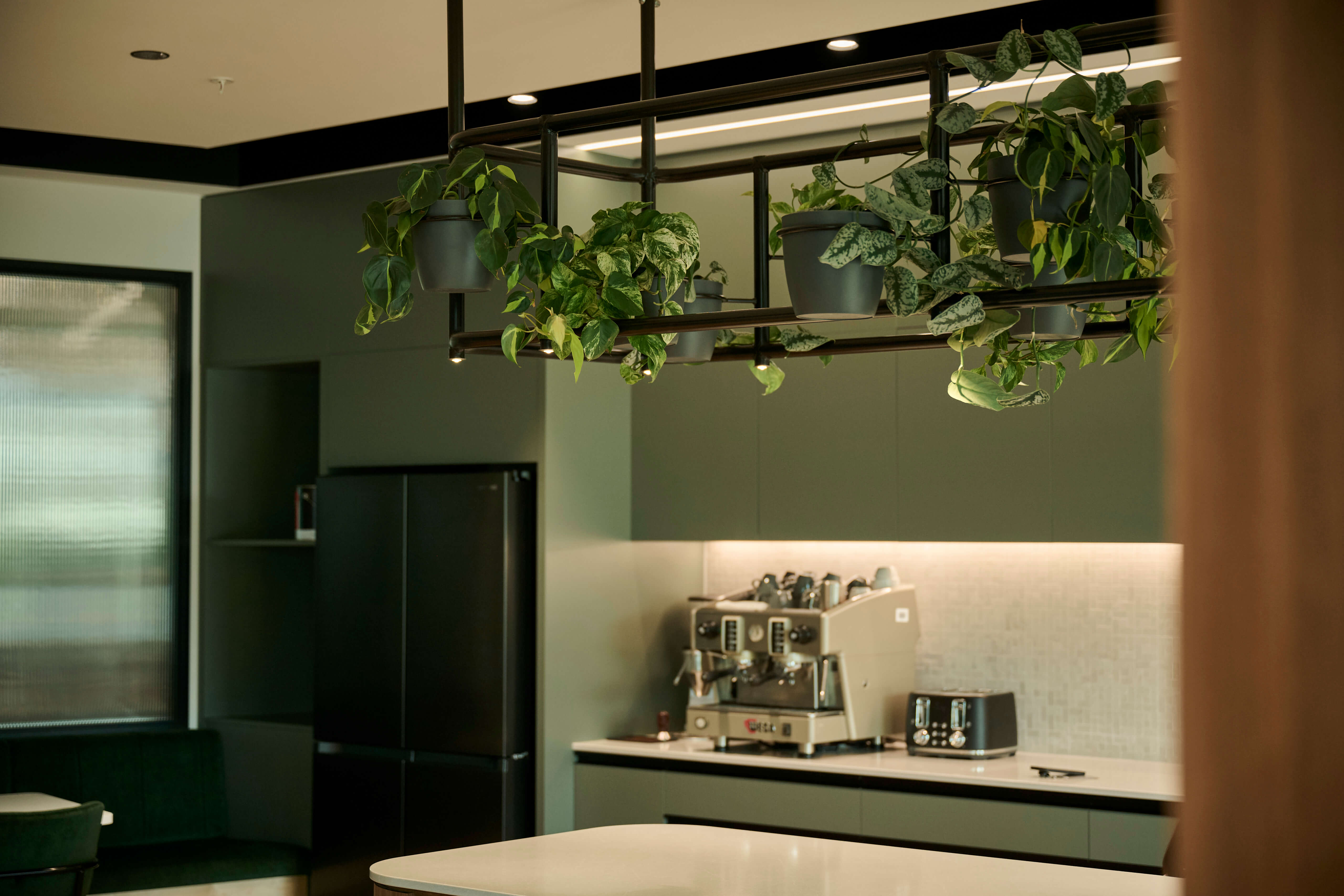 Close-up of a custom hanging planter rack with trailing pothos and philodendron above a kitchen counter.