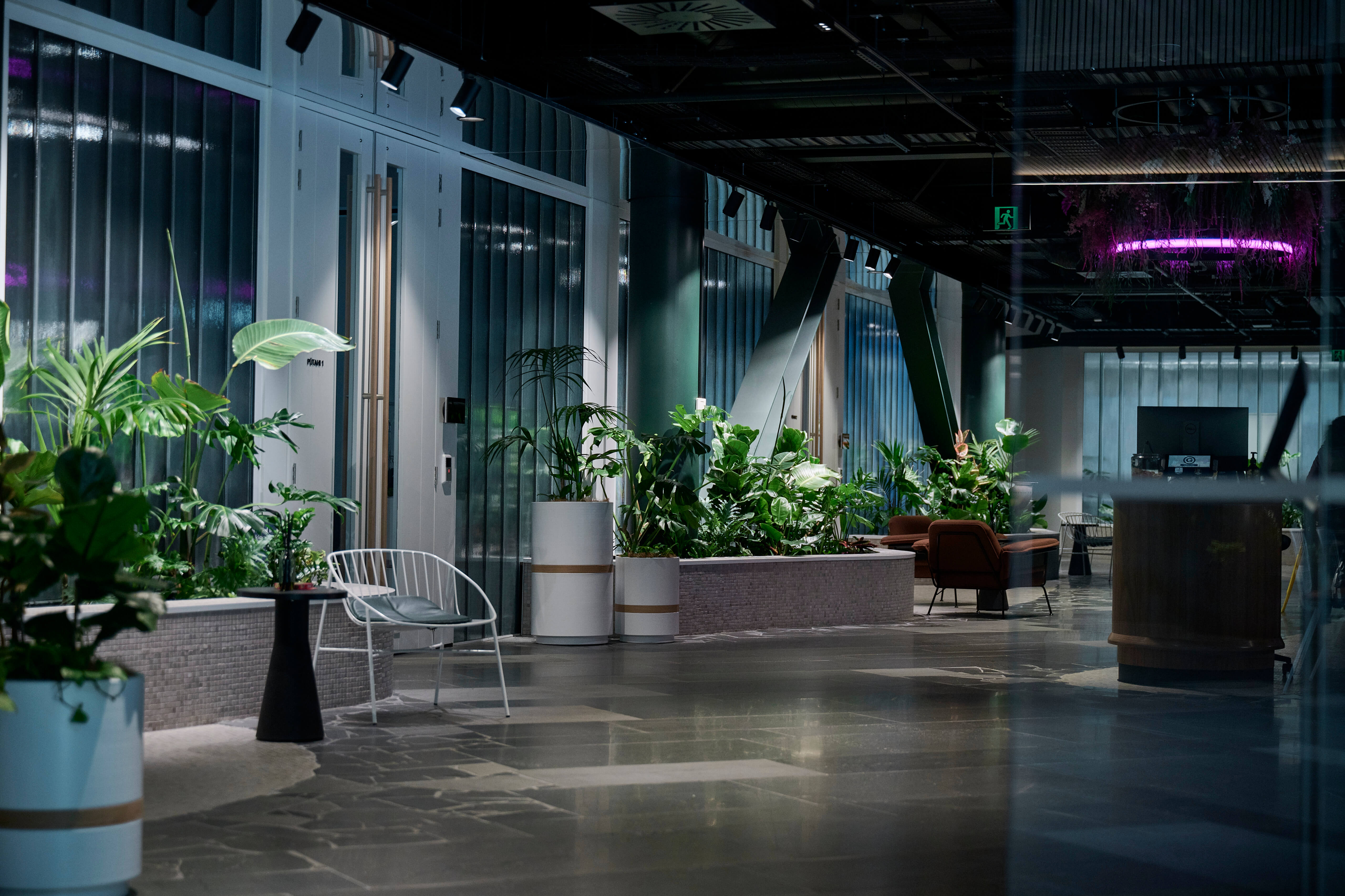 Ground floor atrium at 44 Bowen Street — planters lining the corridor between teal glass partitions and an exposed ceiling.