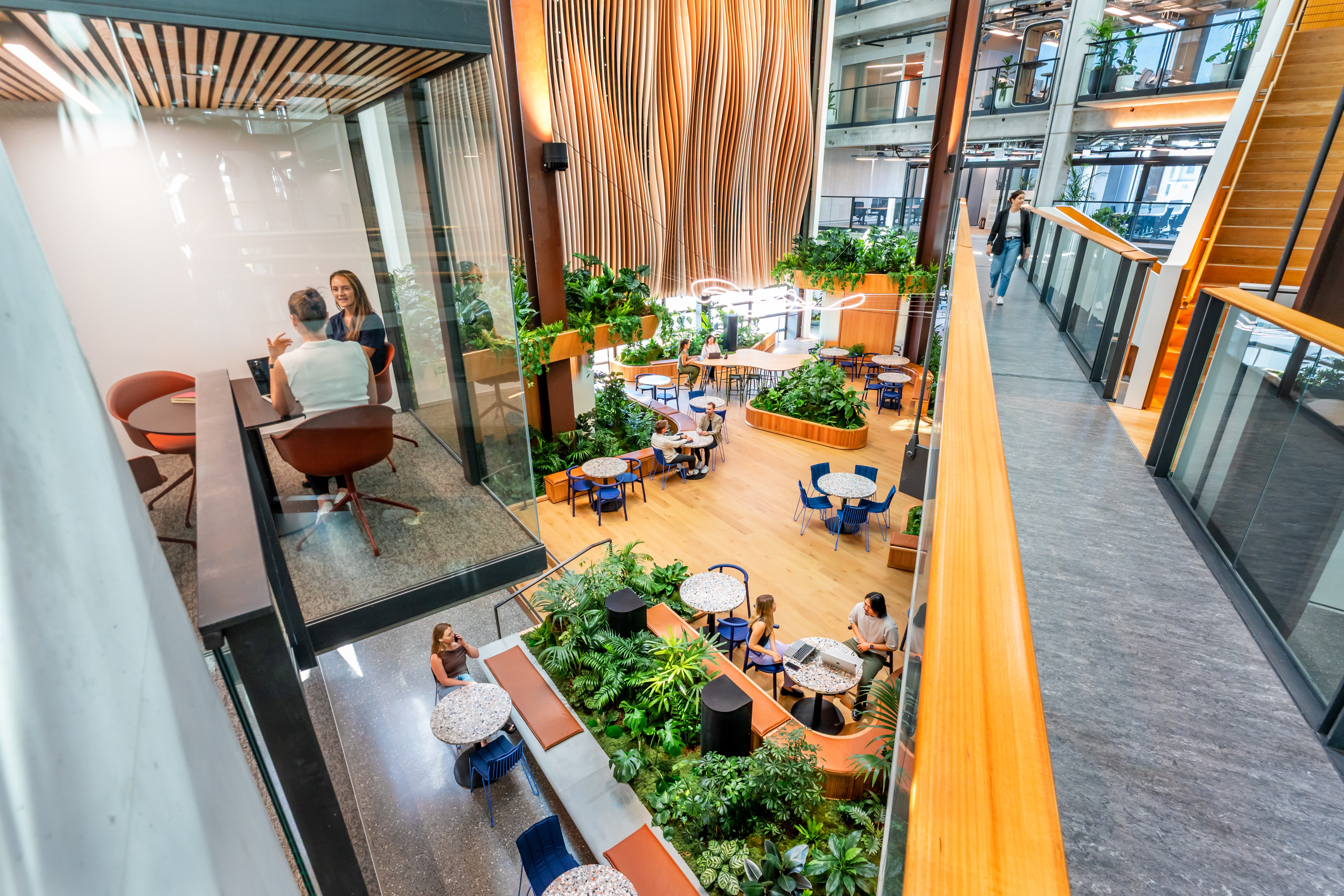 An overhead view of B:HIVE's atrium — curved planter benches and tropical planting across multiple connected levels.