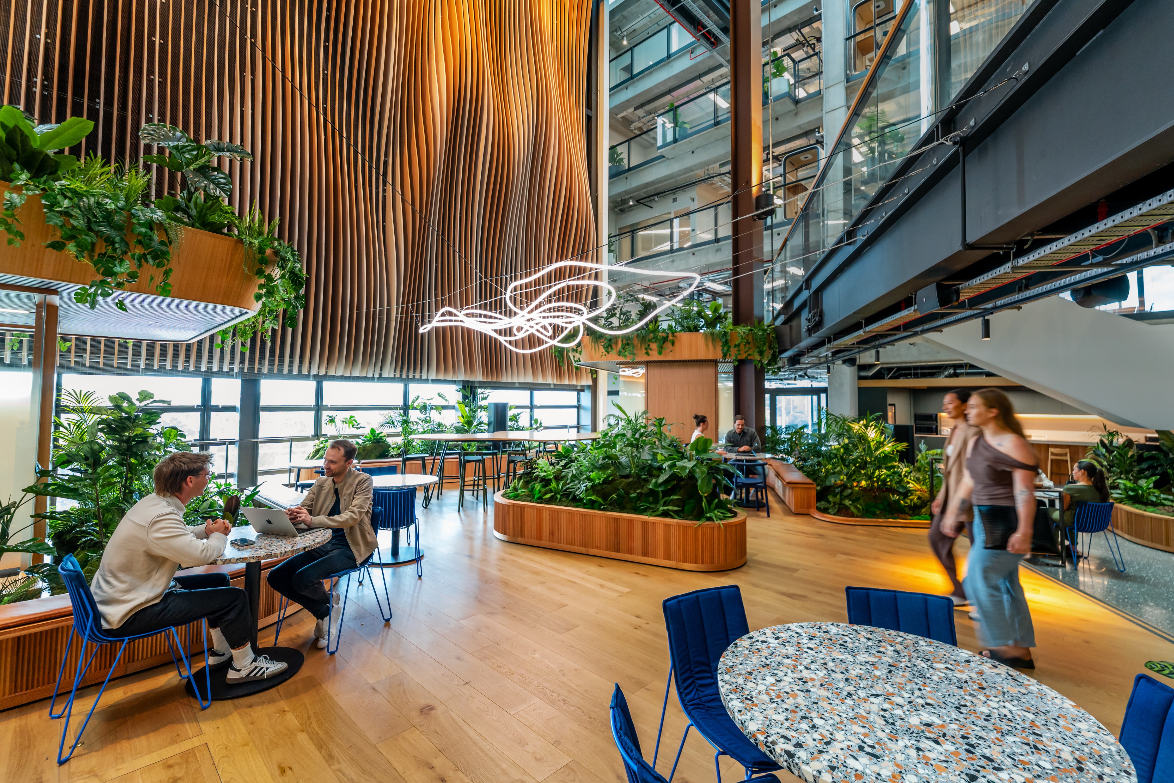 Curved timber planter benches with lush tropical planting define the communal hub at B:HIVE Smales Farm.