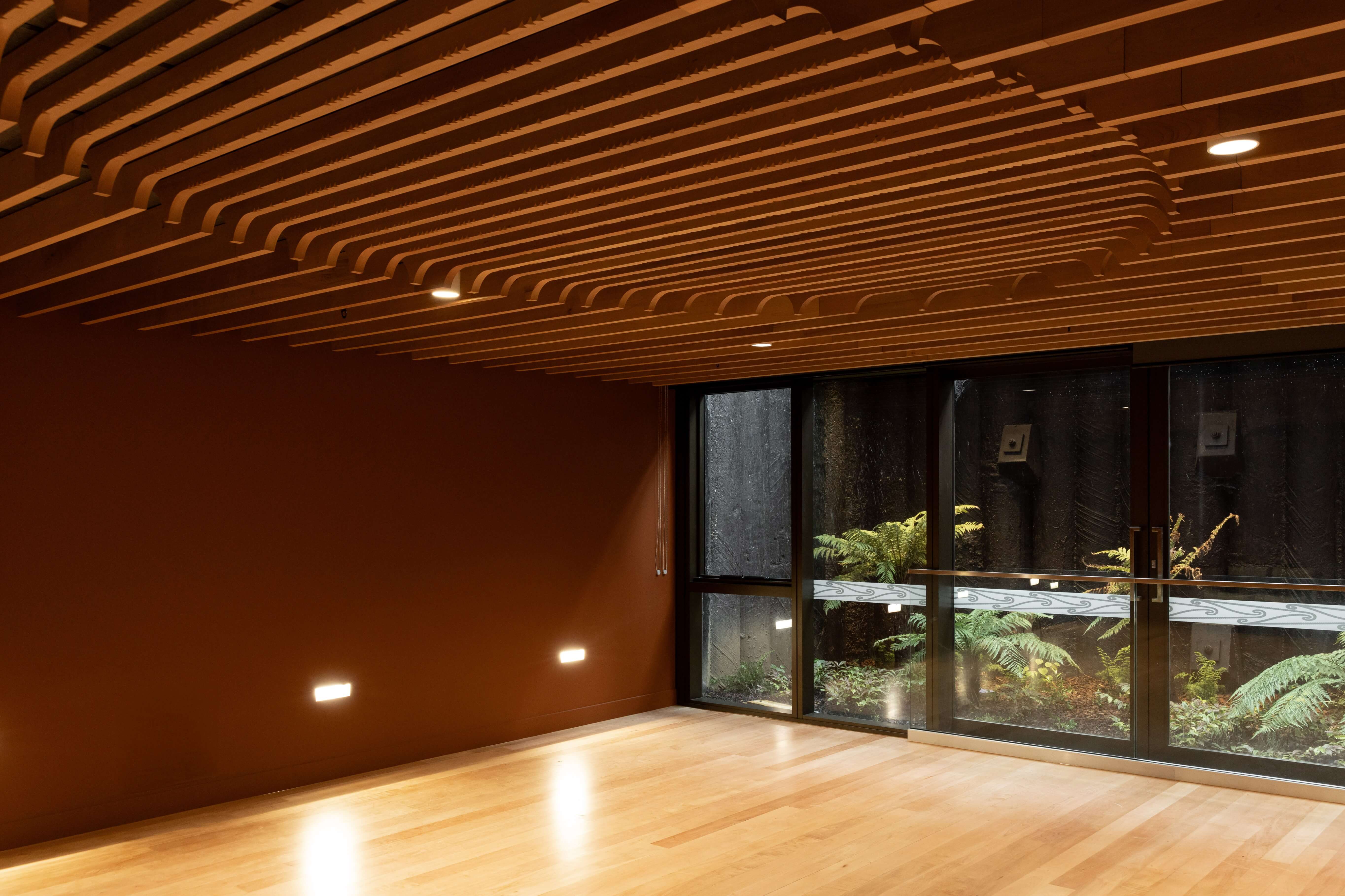 Wave-form timber-slatted ceiling above a room opening onto a fern-planted courtyard with a carved timber balustrade.