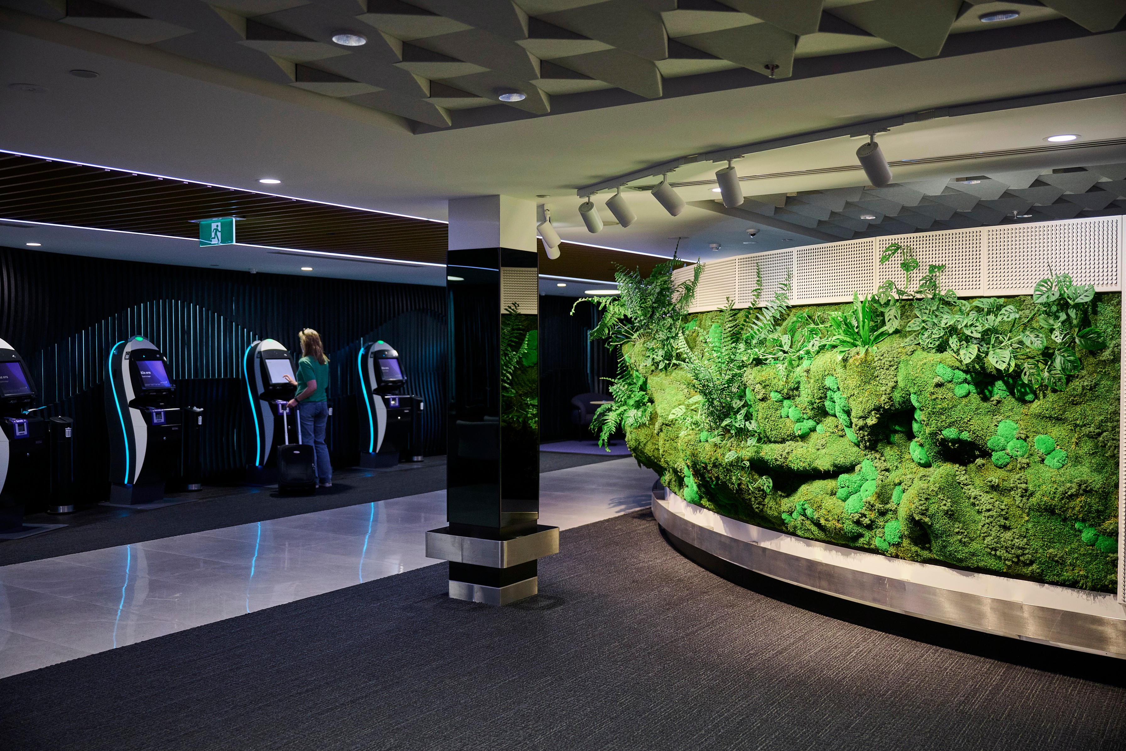 Curved Forest Wall rising behind Air New Zealand's self-check-in kiosks at Auckland Airport, layered with ferns and moss.
