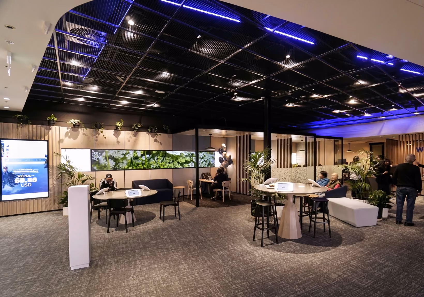 BNZ New Lynn banking floor with staff at high tables, Kentia palms and wall-mounted trailing plants against timber panelling.