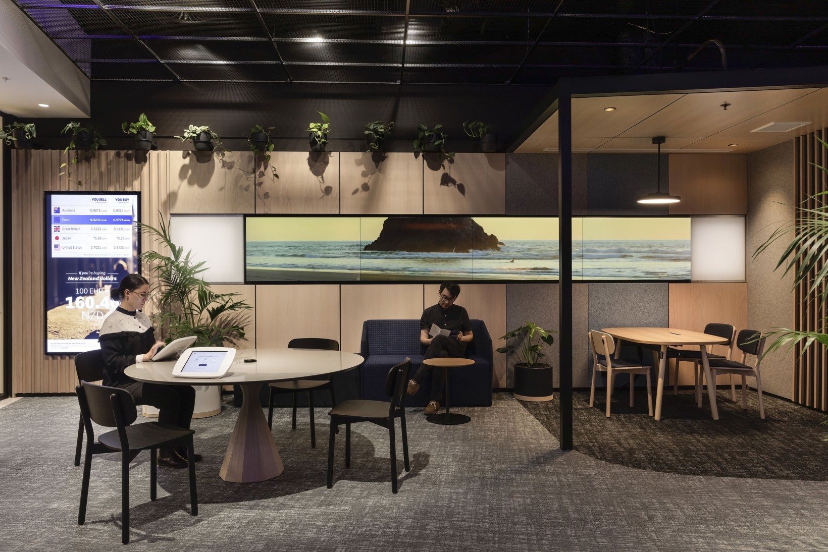 Bank lounge seating area with palms and wall-mounted trailing plants beneath a landscape screen display.