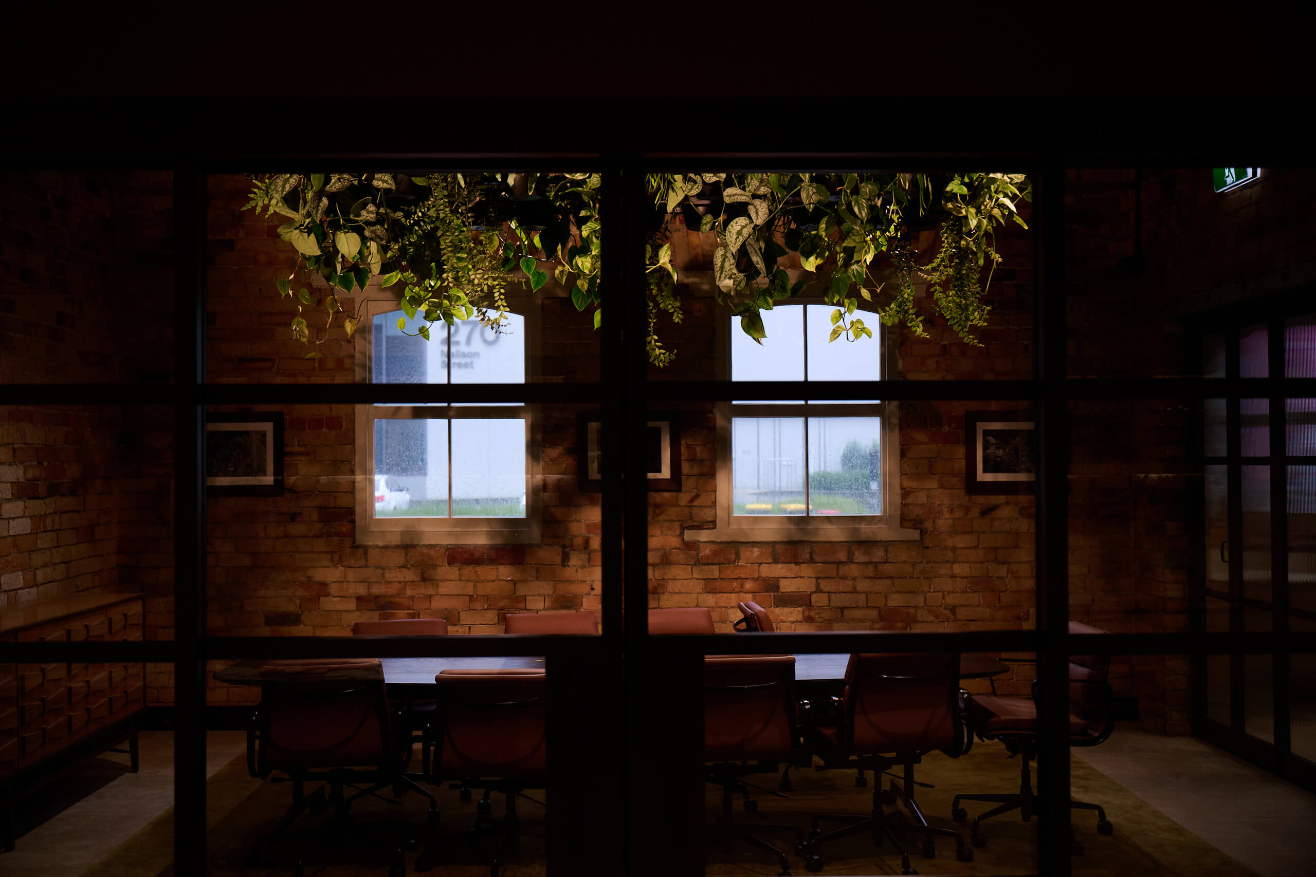 Trailing plants cascade from the ceiling above the meeting room at Gold Merchants, glimpsed through the glass partition.