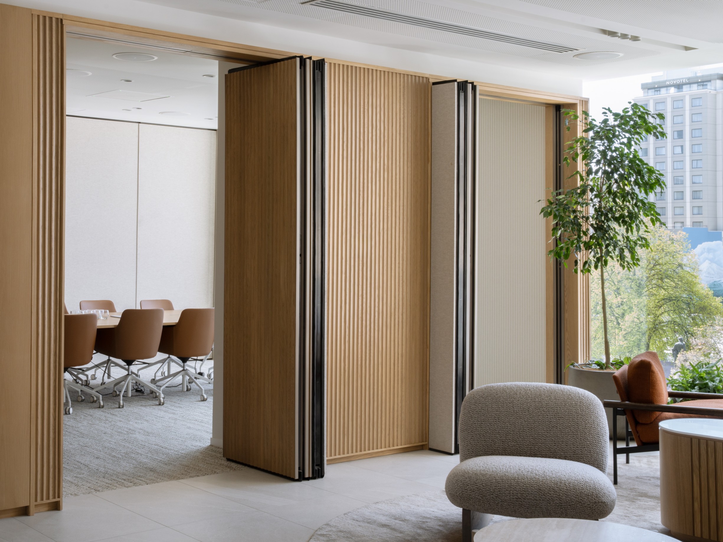 Ficus benjamina in a round planter beside lounge seating and a folding timber-slat meeting room partition.