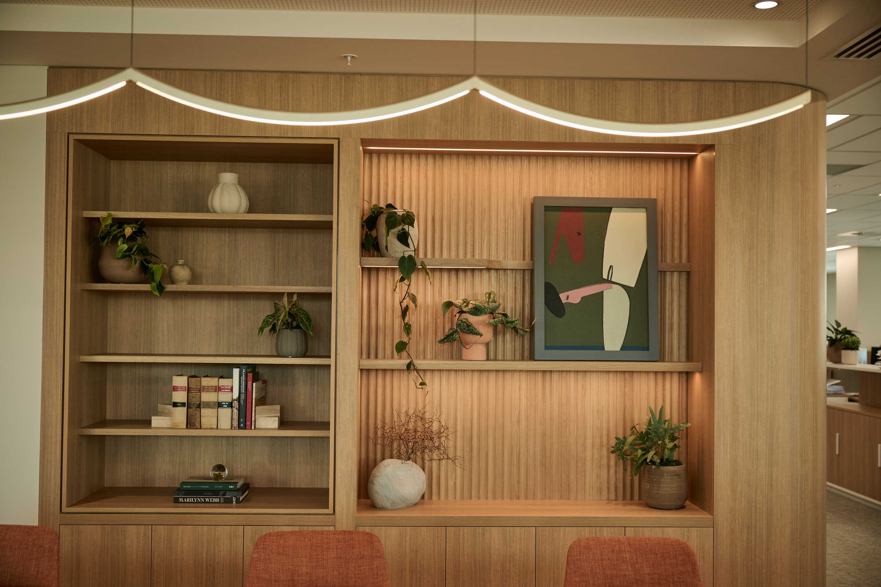 Styled timber shelving with trailing pothos, potted foliage, law books and artwork above terracotta chairs.