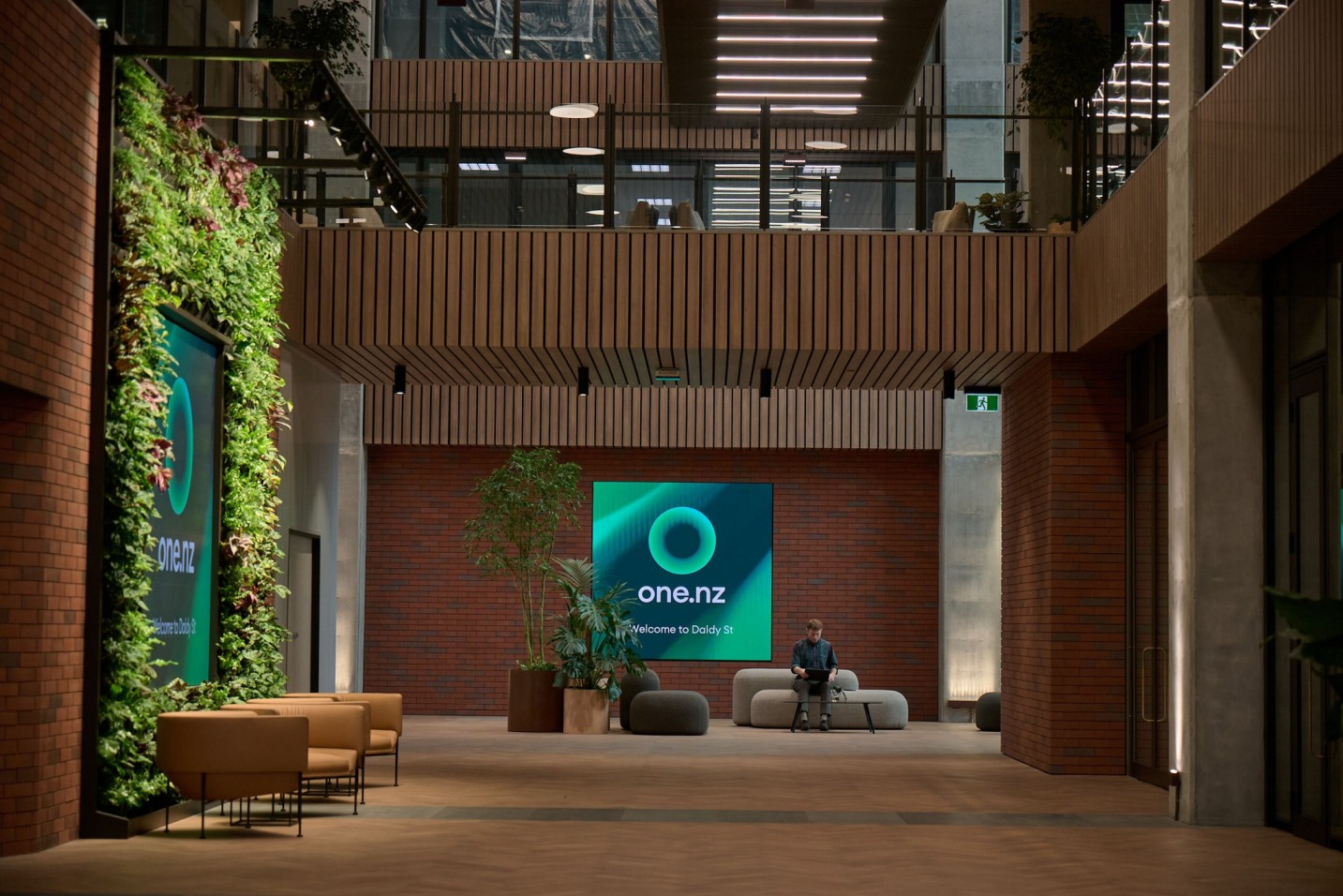 A green wall and potted trees flank the One NZ welcome screen in a brick atrium at 30 Daldy Street.