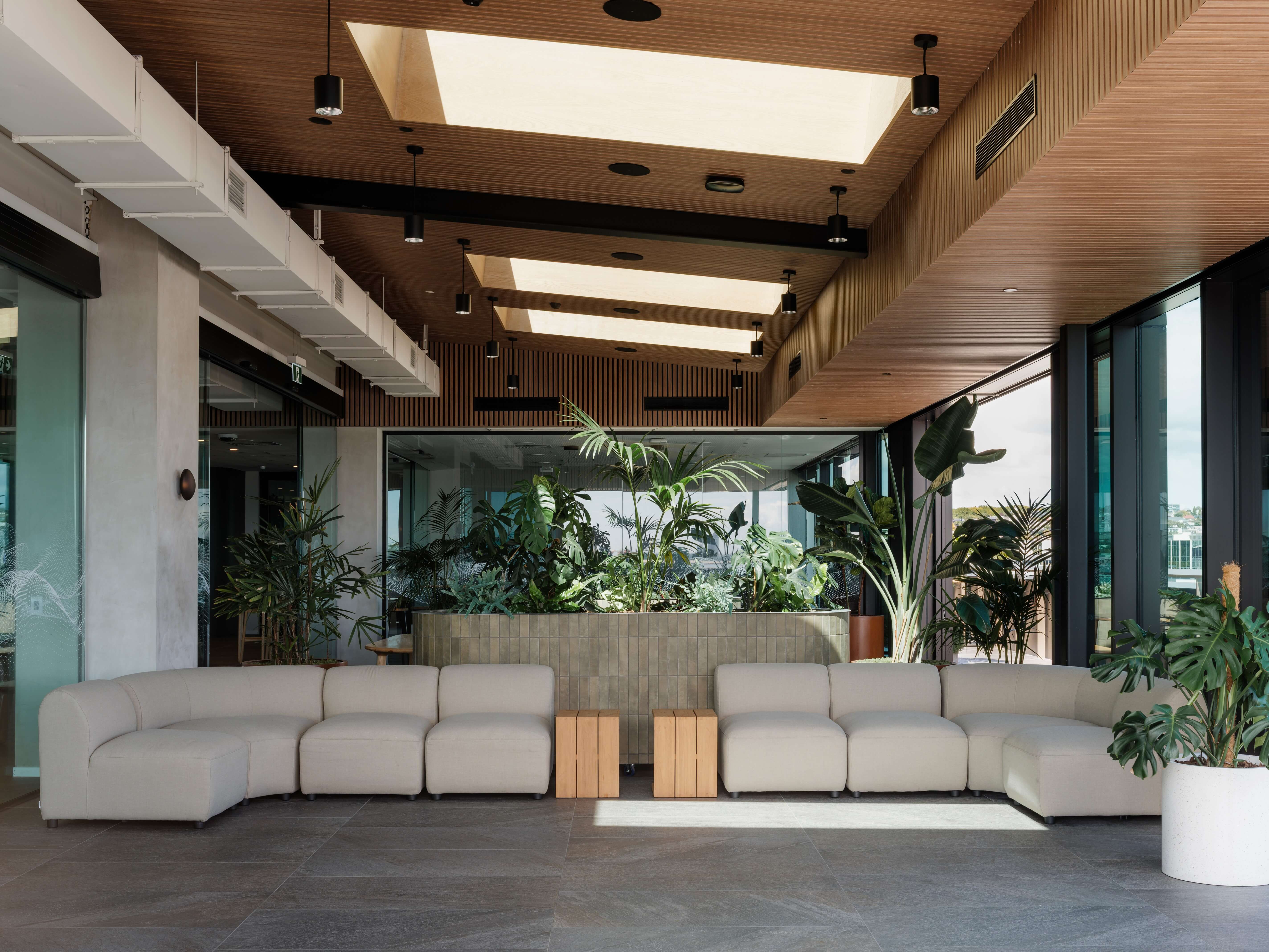 Curved banquette seating with round timber café tables and chairs, densely planted along the top of the seat back.