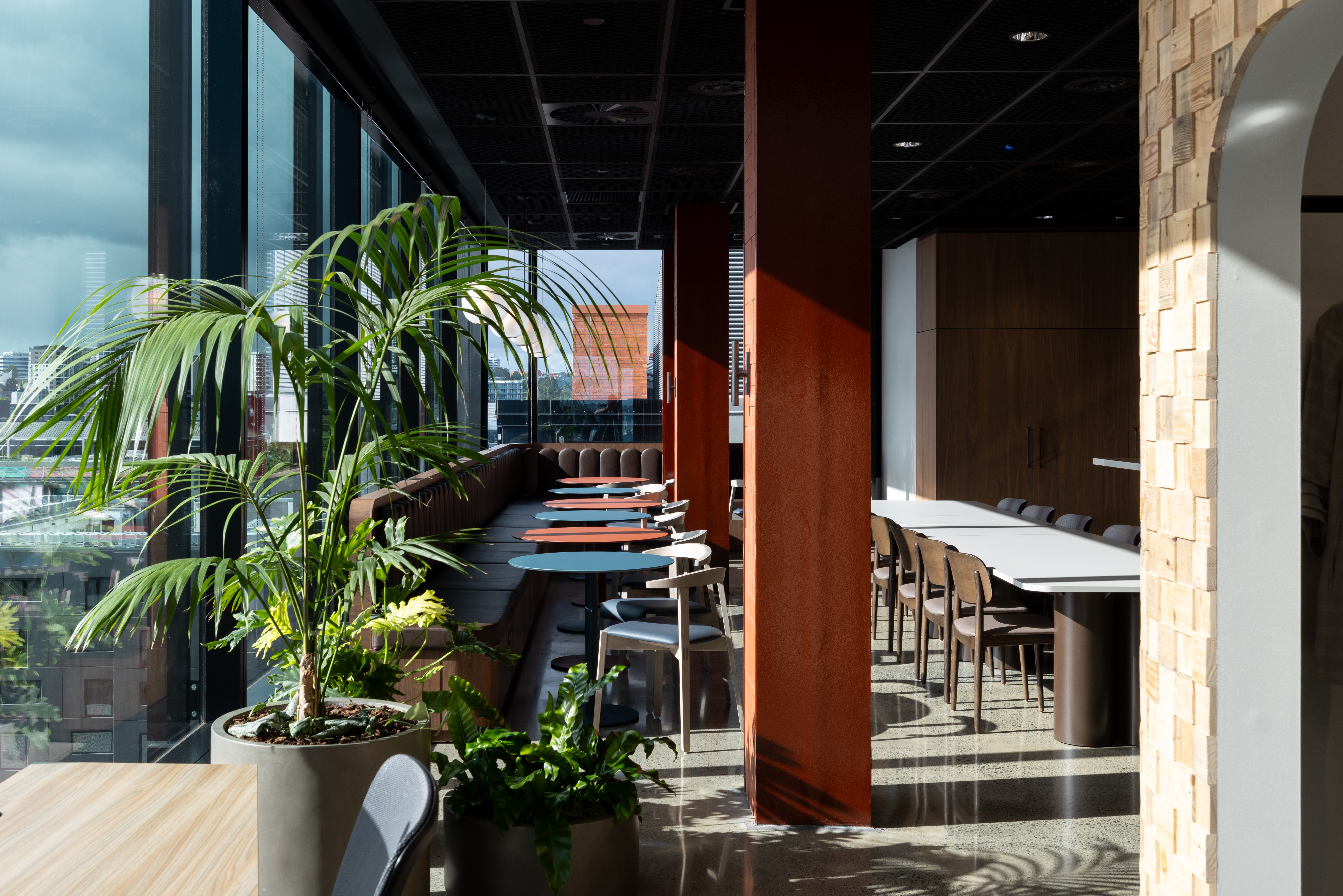 Palms and bistro seating along a breakout corridor with harbour views and a timber archway beyond.