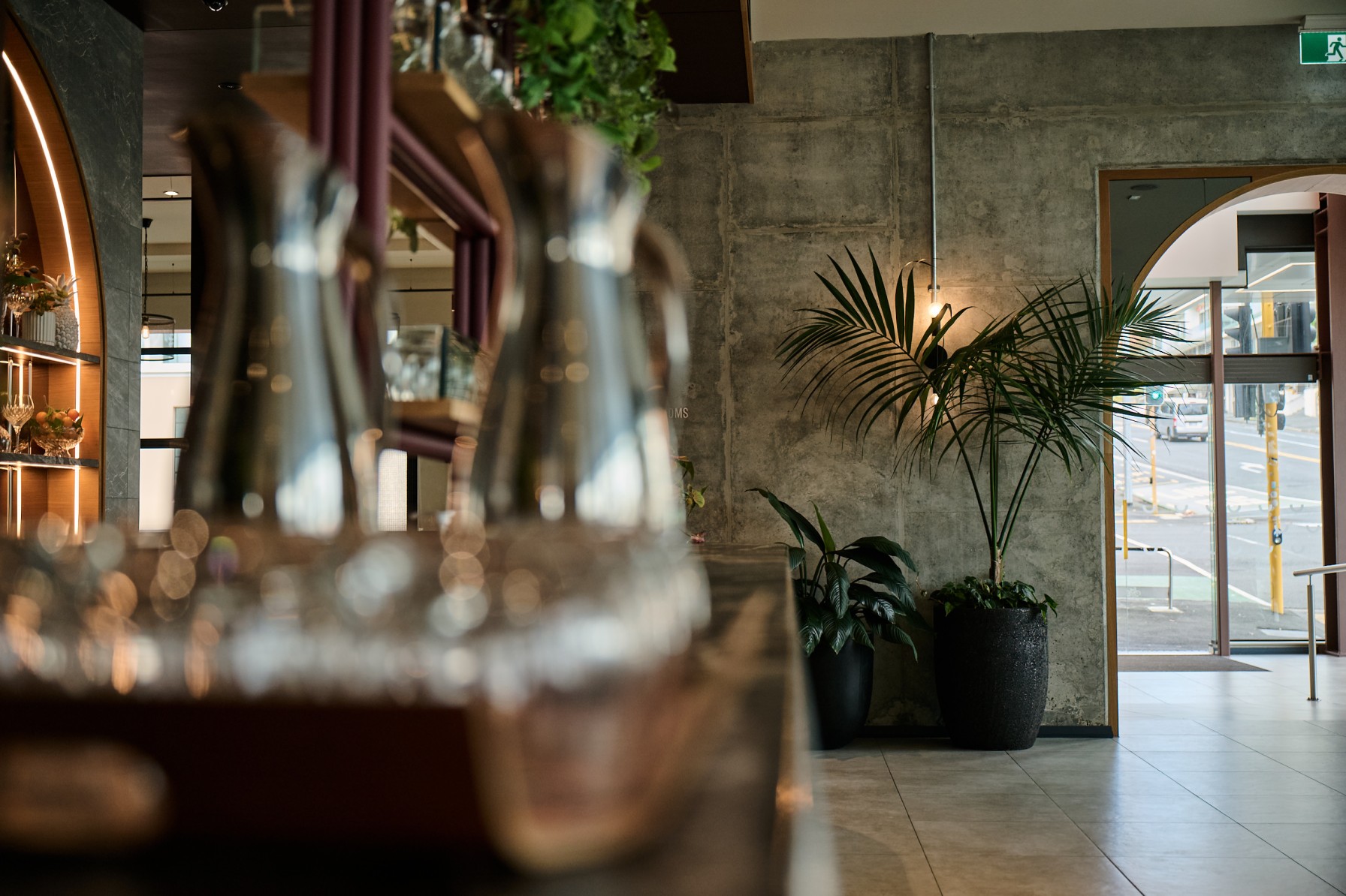 Kentia palms in dark planters flank the arched hotel entrance at Sudima Auckland, seen from the restaurant.