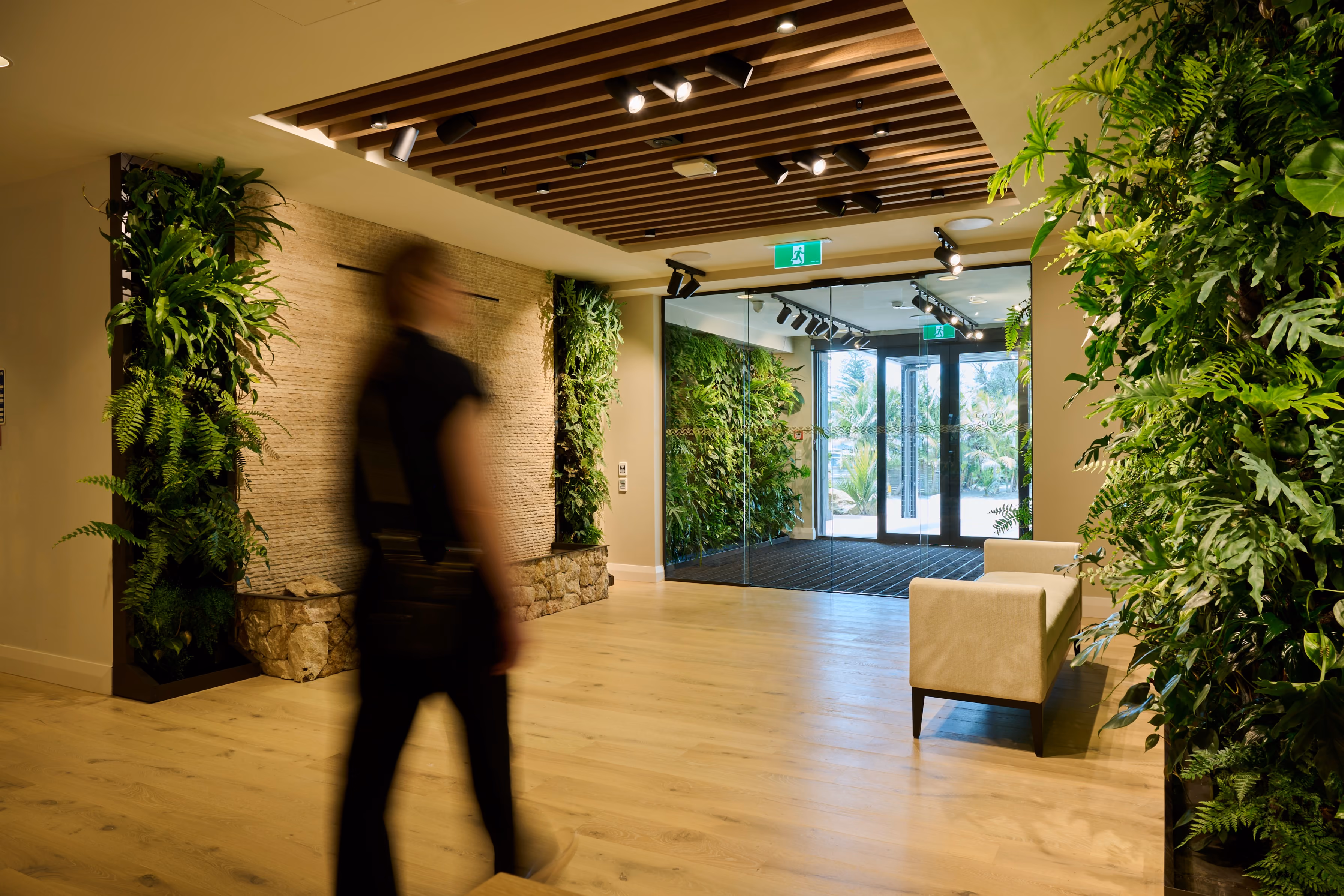 A resident walks through Orewa's lobby, flanked by lush living walls of ferns and tropical foliage.