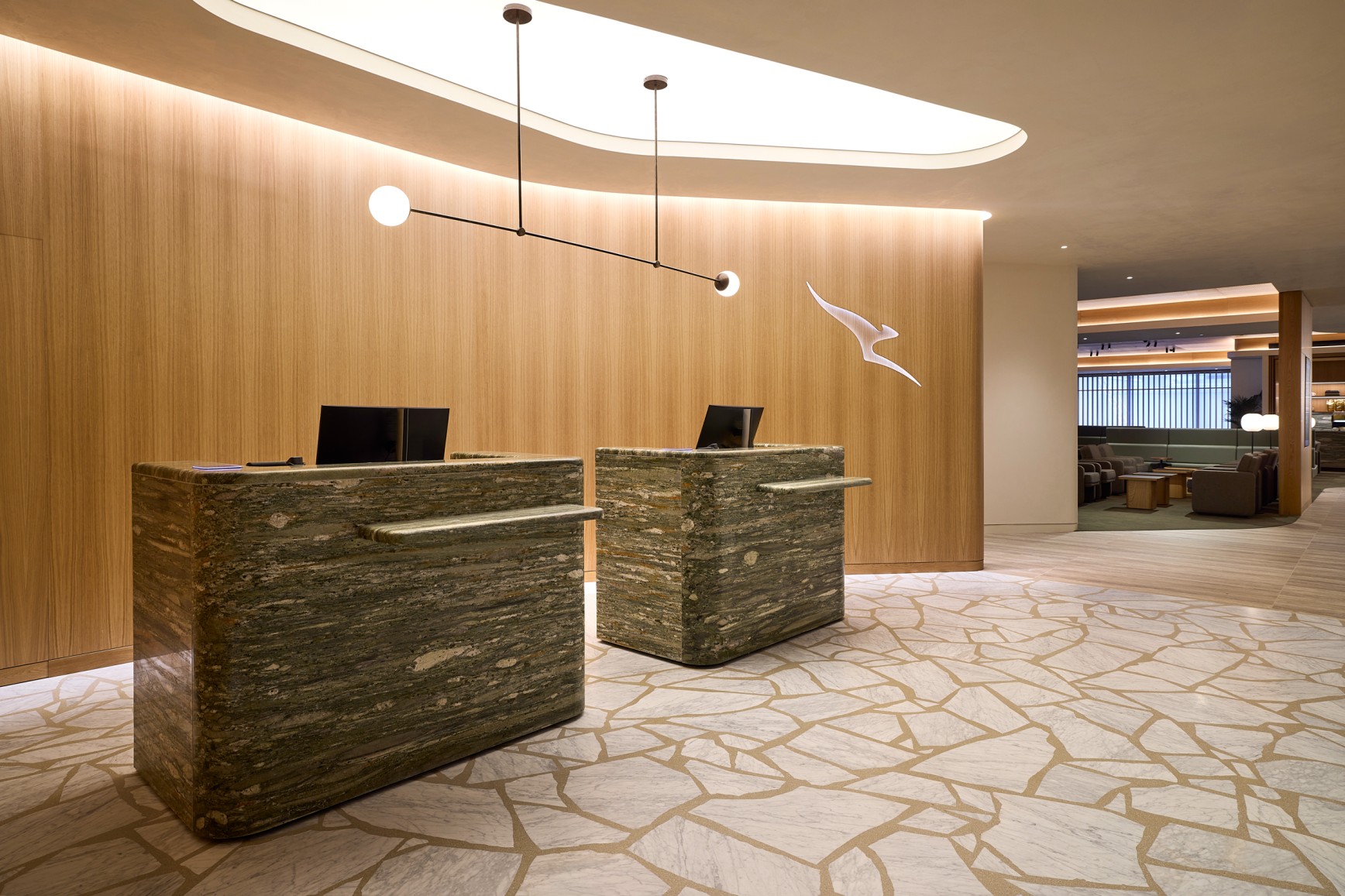 Qantas Business Lounge reception at Auckland Airport — marble desks and warm timber walls with greenery beyond.