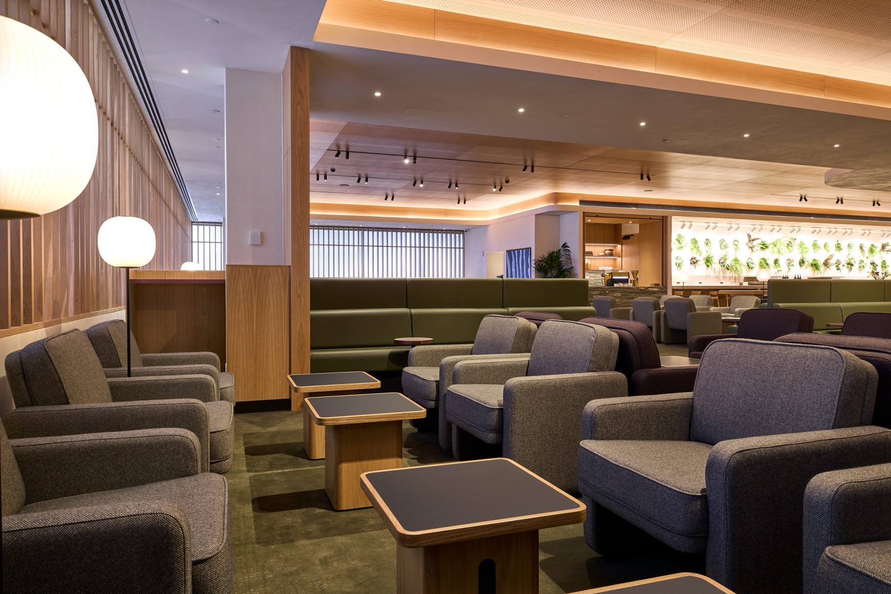 Qantas Business Lounge reception at Auckland Airport — marble desks and warm timber walls with greenery beyond.