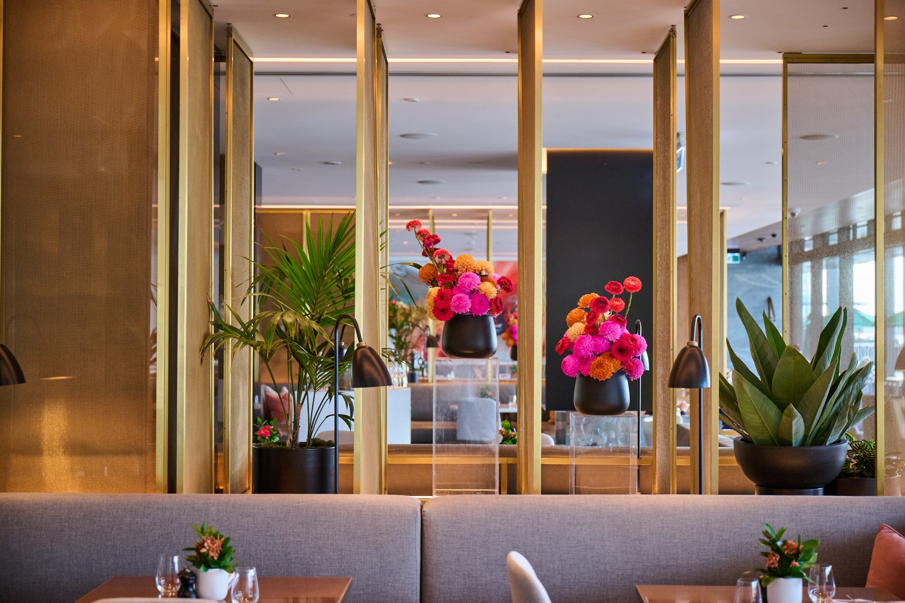 Vivid floral arrangements and a kentia palm enliven Park Hyatt Auckland's restaurant, behind brass-edged glass partitions.