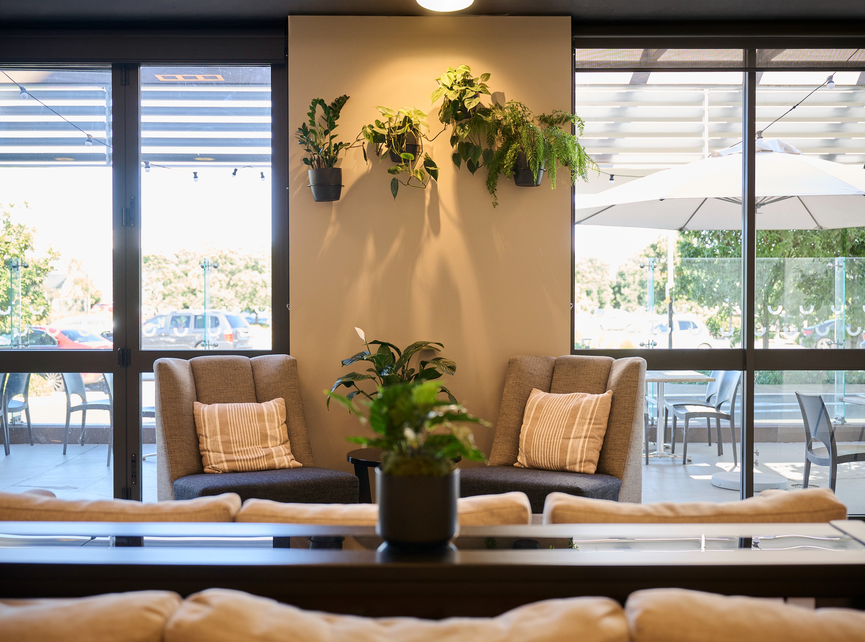 Wall-mounted trailing pothos and fern planters above a peace lily on a side table between wingback lounge chairs.