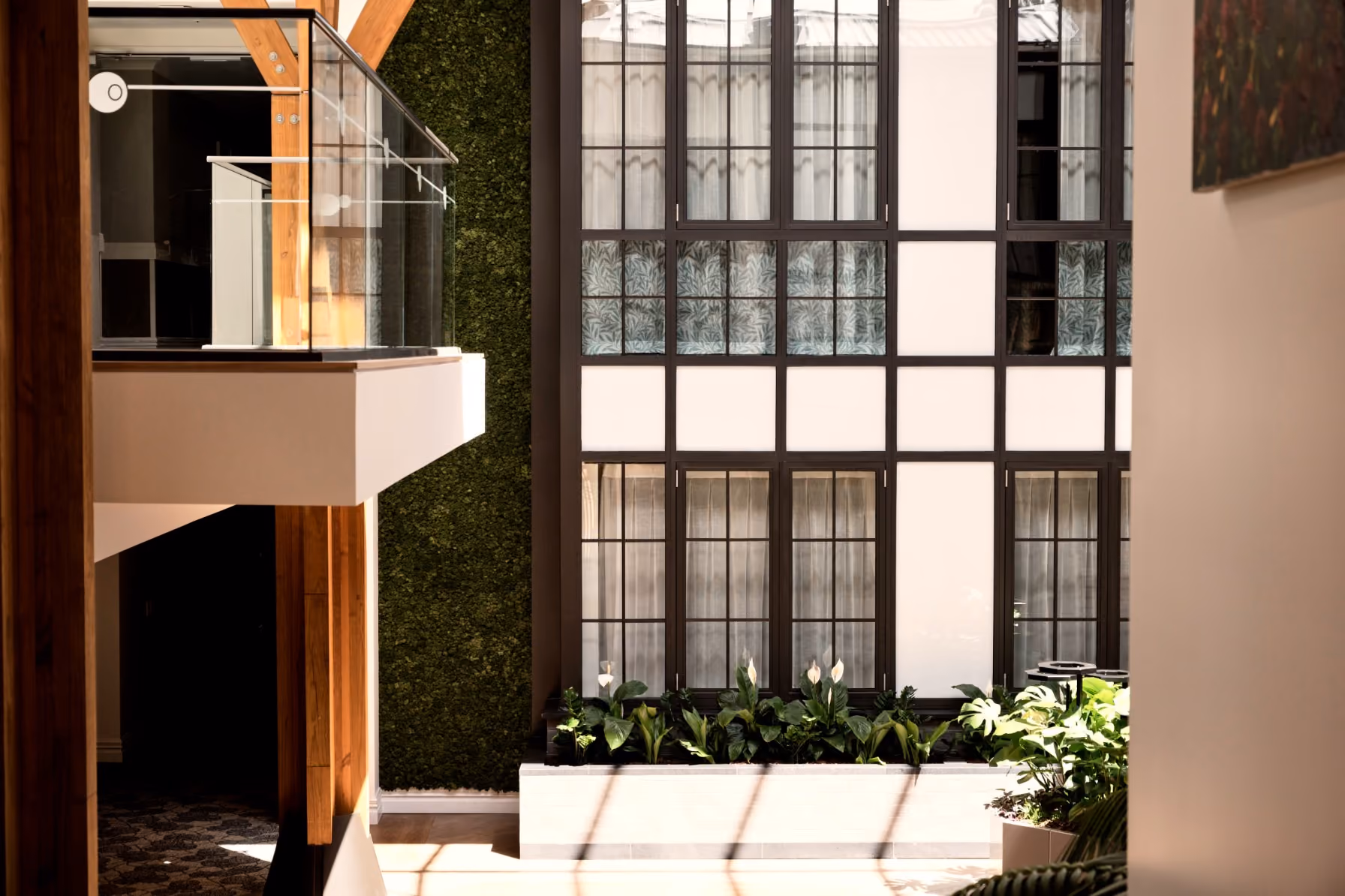 Green wall and glass mezzanine balcony overlooking a lit staircase and artwork in the multi-storey atrium.