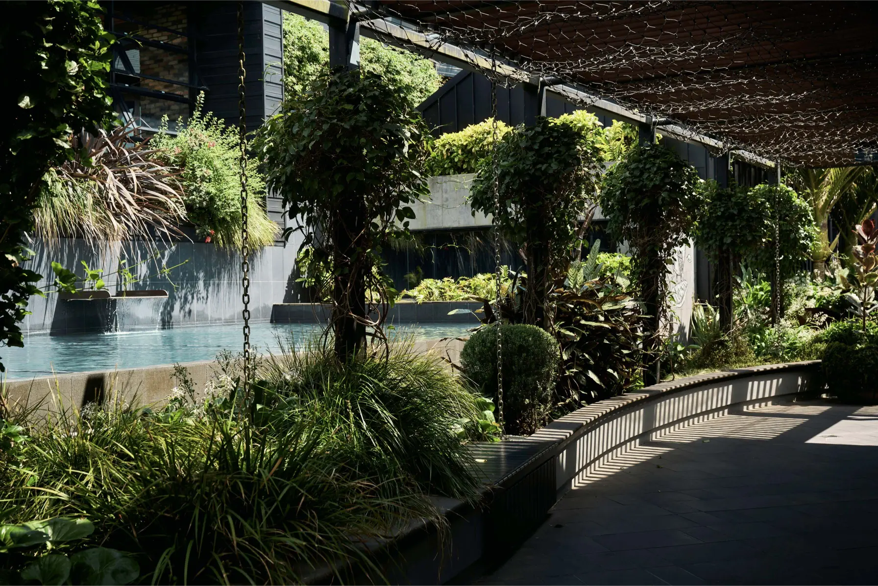 Westfield's shaded courtyard garden with a reflecting pool, water feature, hanging plants, and a curved bench along a paved walkway