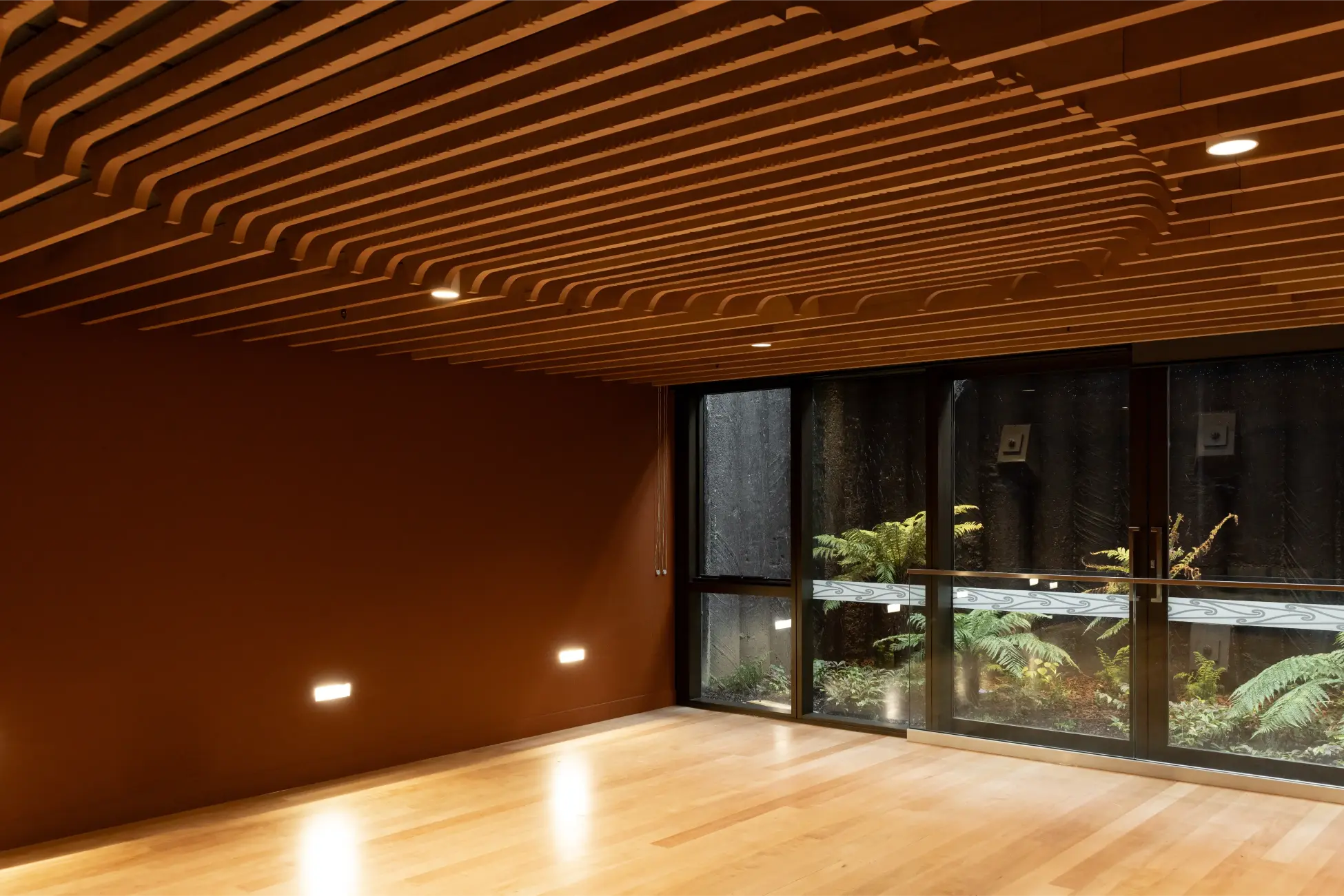 Wave-form timber-slatted ceiling above a room opening onto a fern-planted courtyard with a carved timber balustrade.