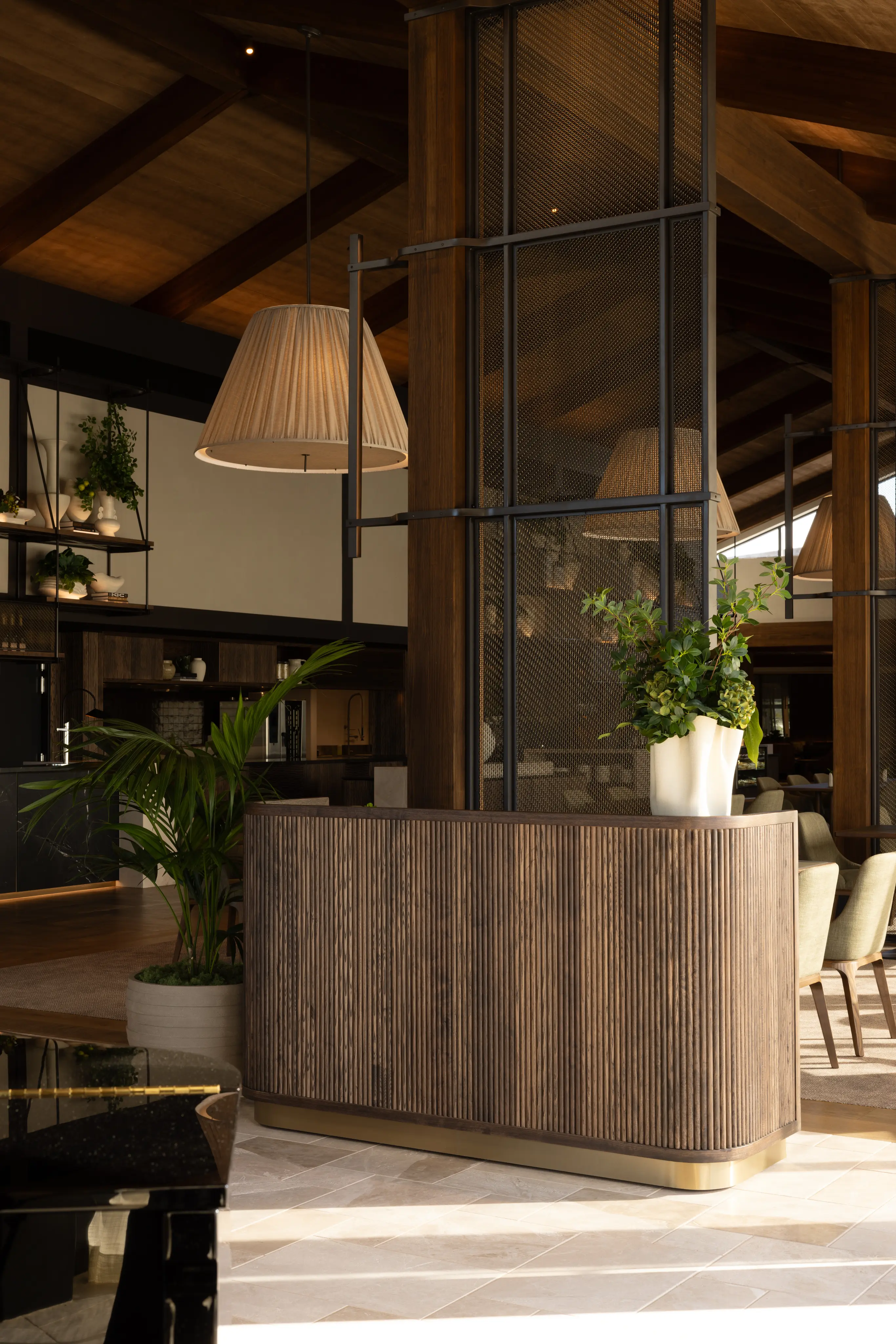 Kentia palm and a foliage arrangement beside a fluted timber bar counter with pendant lighting above.