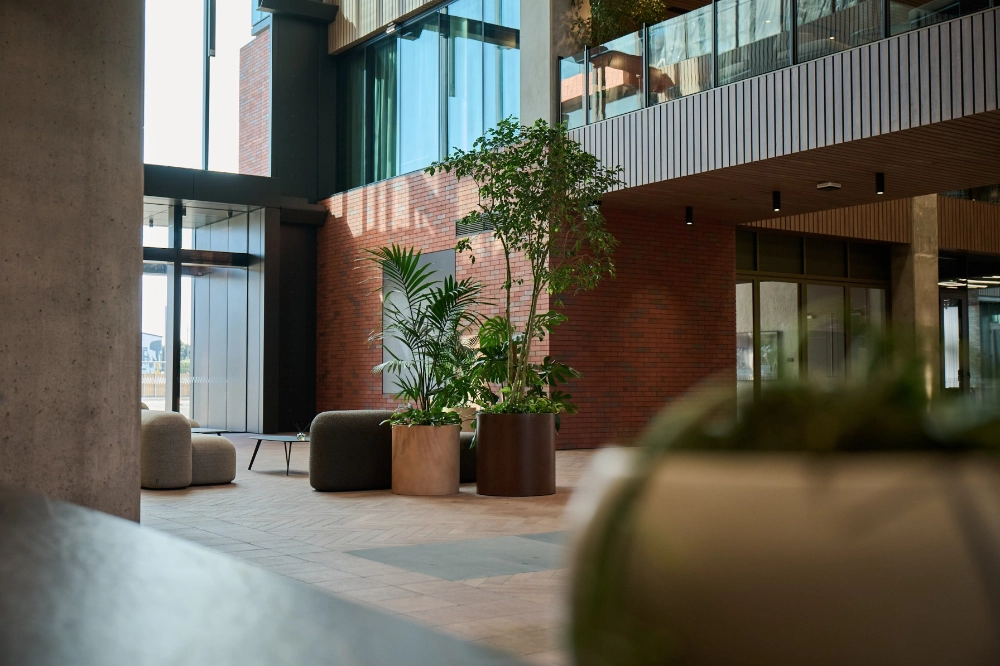 Potted trees and palms in timber planters among lounge seating in a double-height brick atrium.