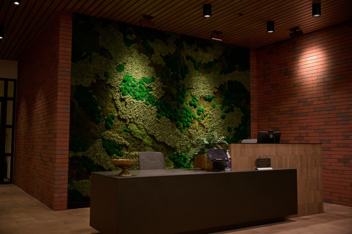 Illuminated moss wall behind the reception desk, set against warm timber and red brick.