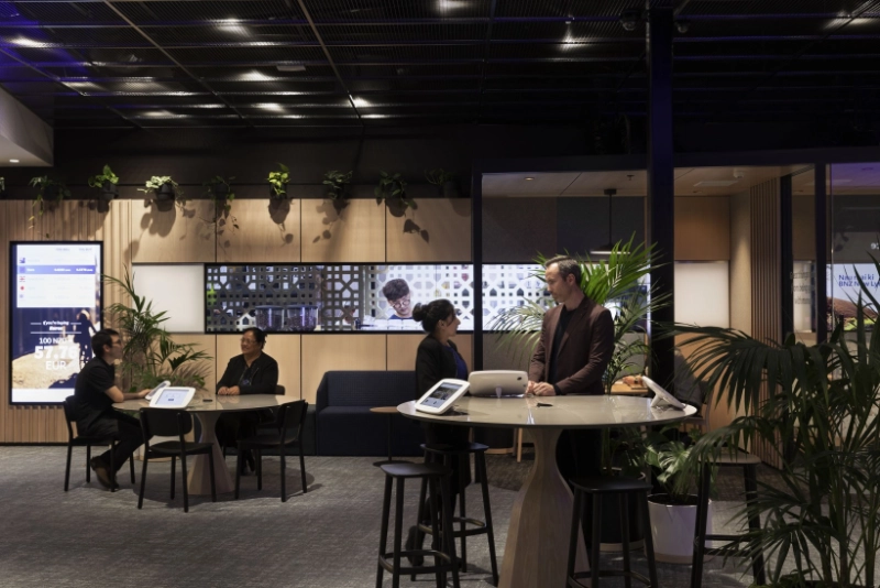 Staff meeting customers at high tables beside Kentia palms, with trailing plants along the timber panelling at BNZ Lynn Mall.