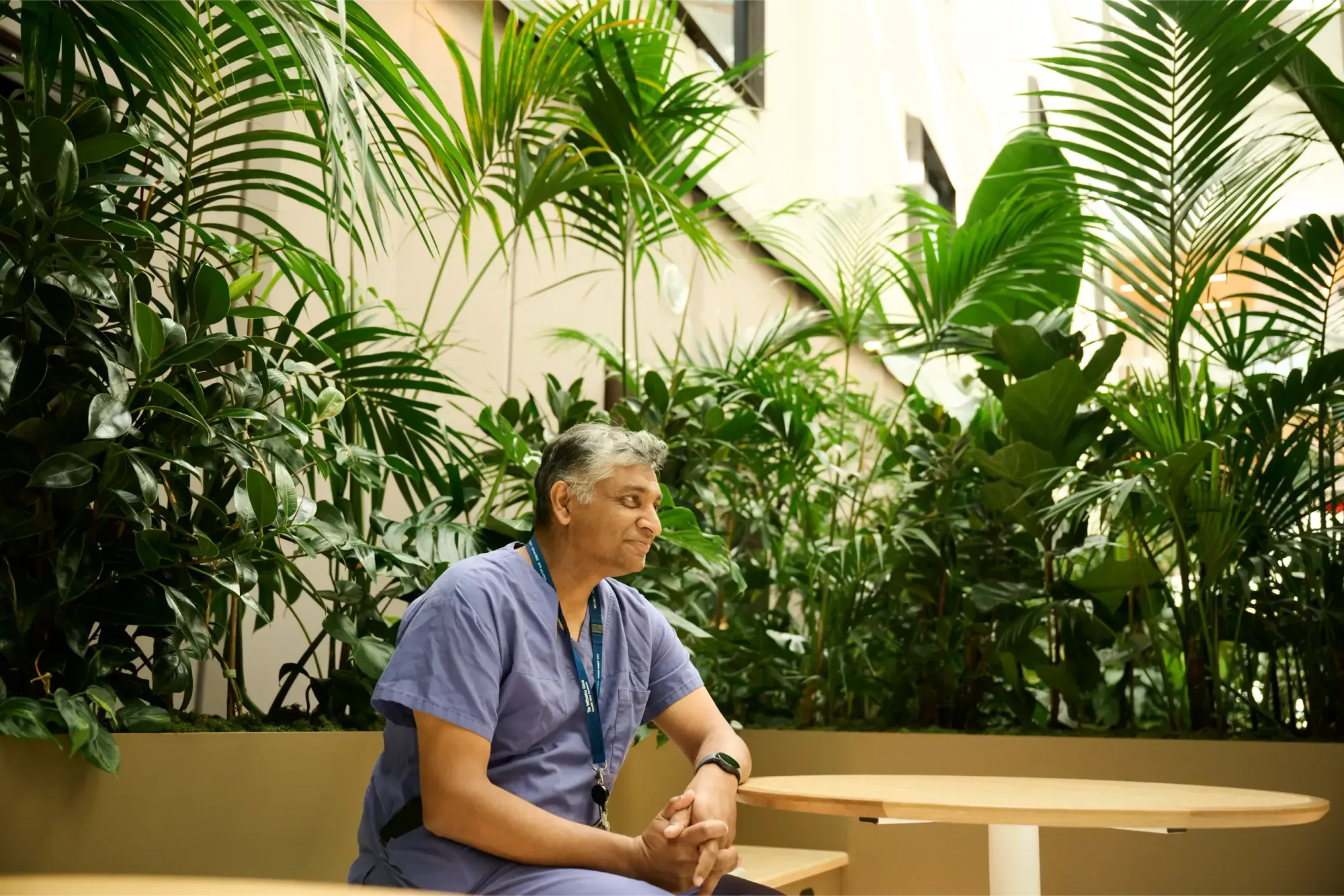 A clinician in scrubs rests at a table surrounded by palms in the Healing Garden