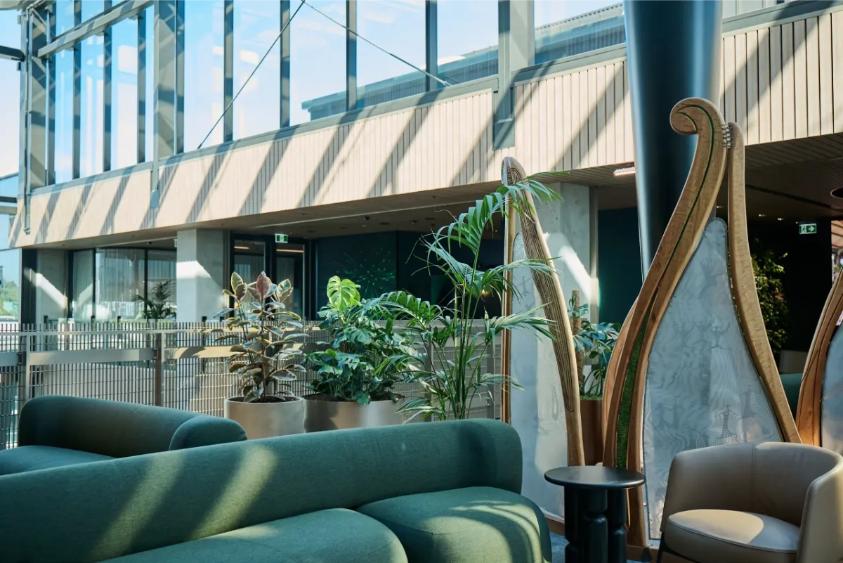 Rubber plants and palms beside green sofas and a glass balustrade at One NZ