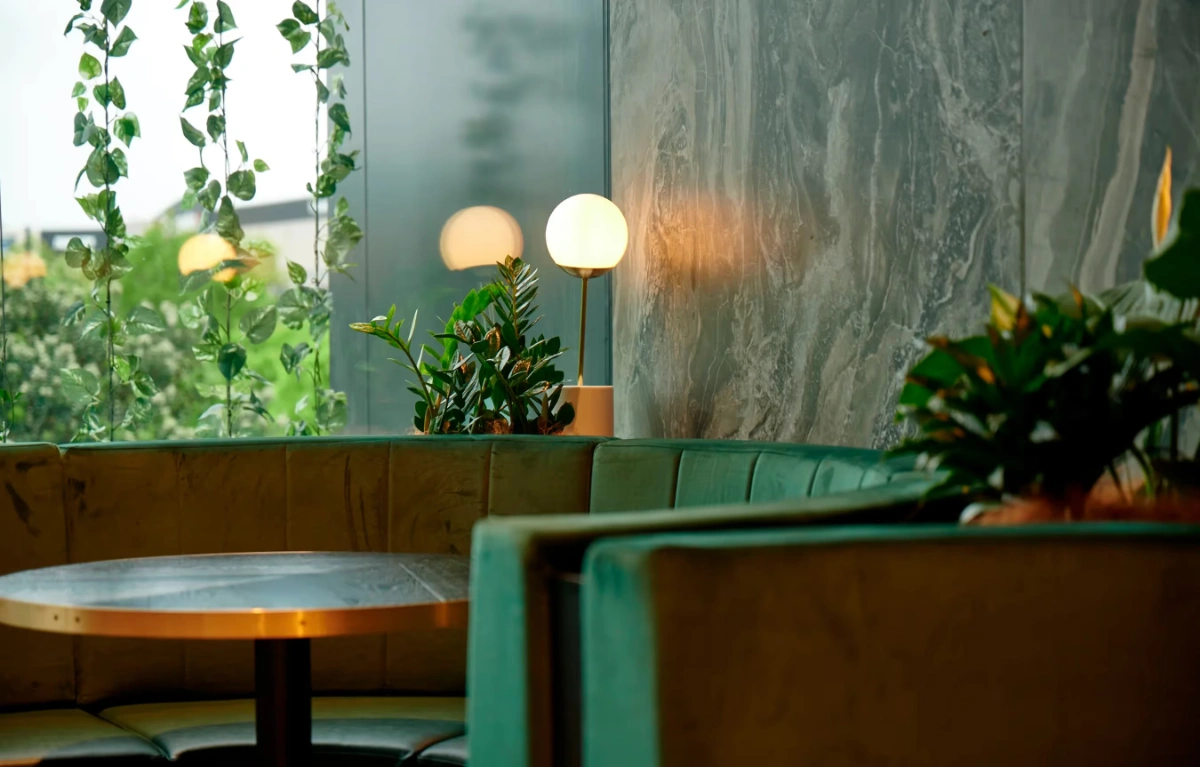 Small plants and trailing greenery around teal booth seating against a marble wall at Sylvia Park