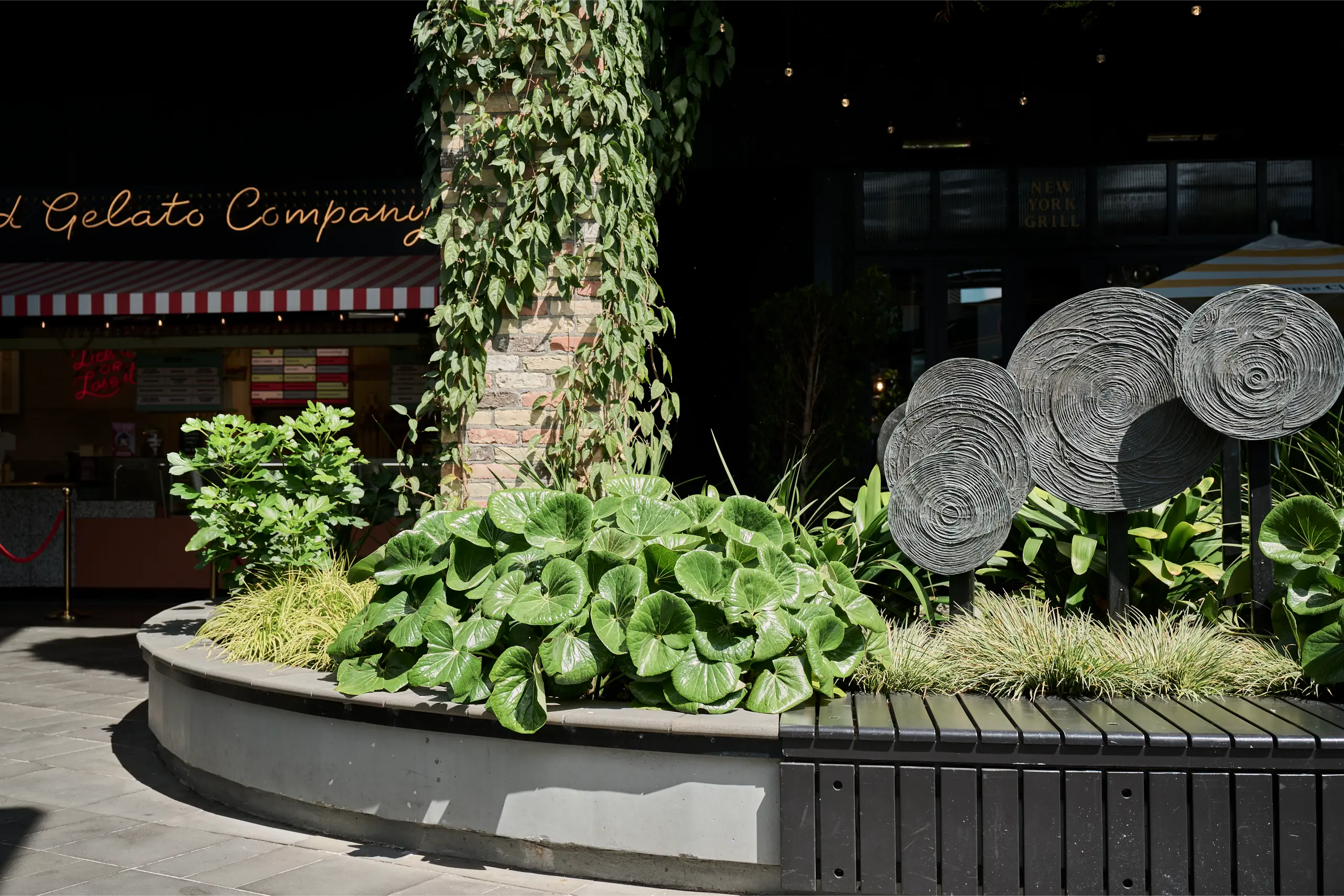 Curved planter of lush foliage with sculptural discs beneath an ivy-covered column