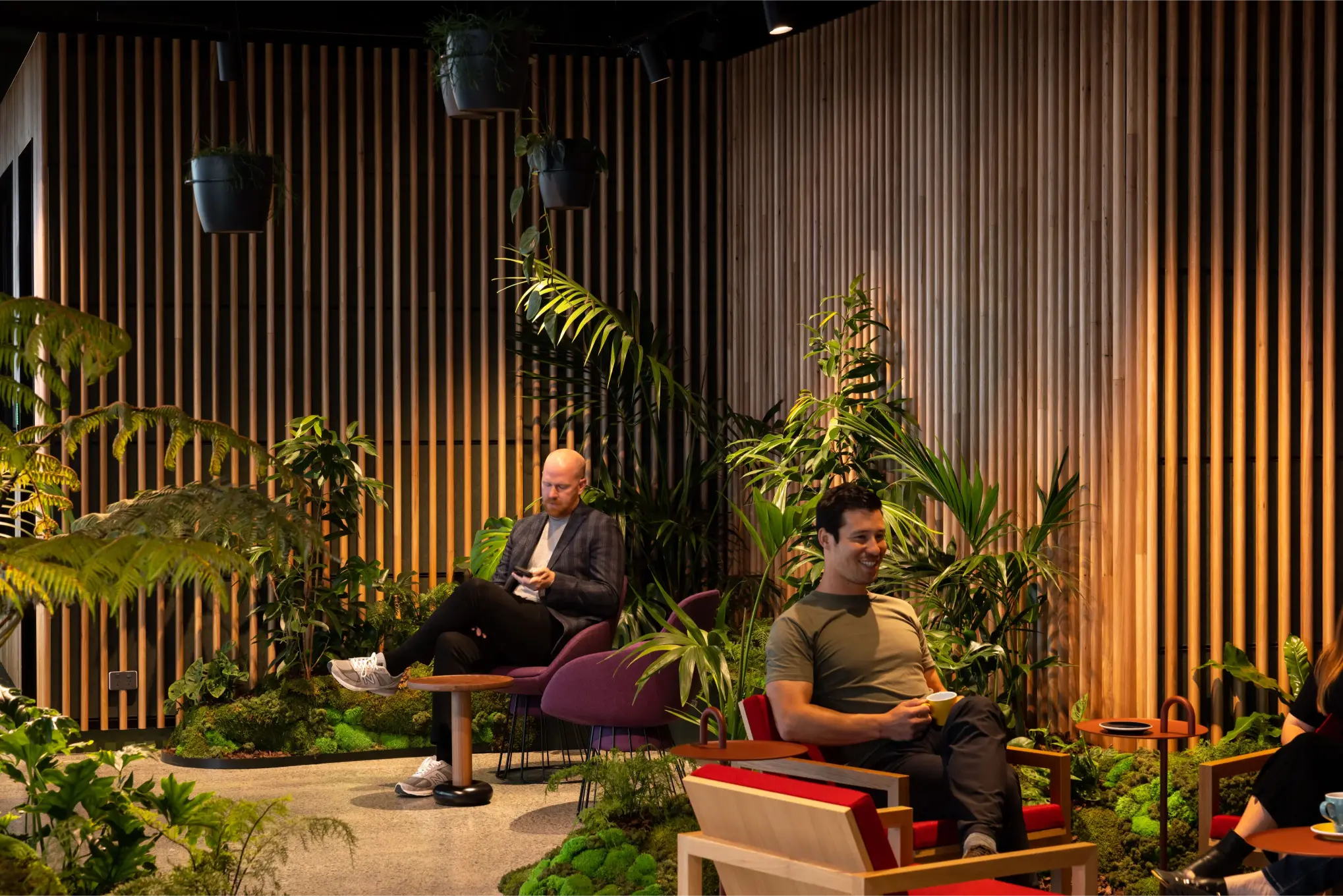 A person checks their phone behind a group of people surrounded by ferns and palms at MC reception area