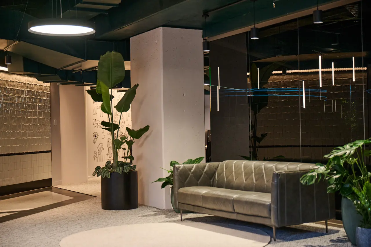 reception/entry, Strelitzia in black planter, leather sofa, illustrated wall): Strelitzia nicolai in a black cylinder planter beside a leather sofa in the Kernal Wealth reception area, with illustrated wall art and moody pendant lighting.