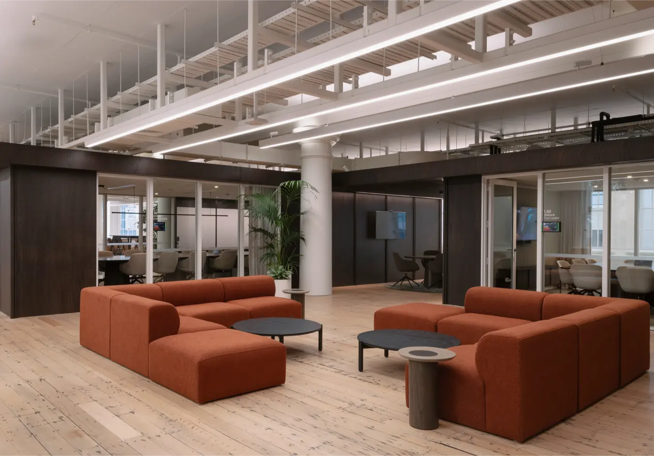 twin rust sofas, meeting rooms behind, industrial ceiling