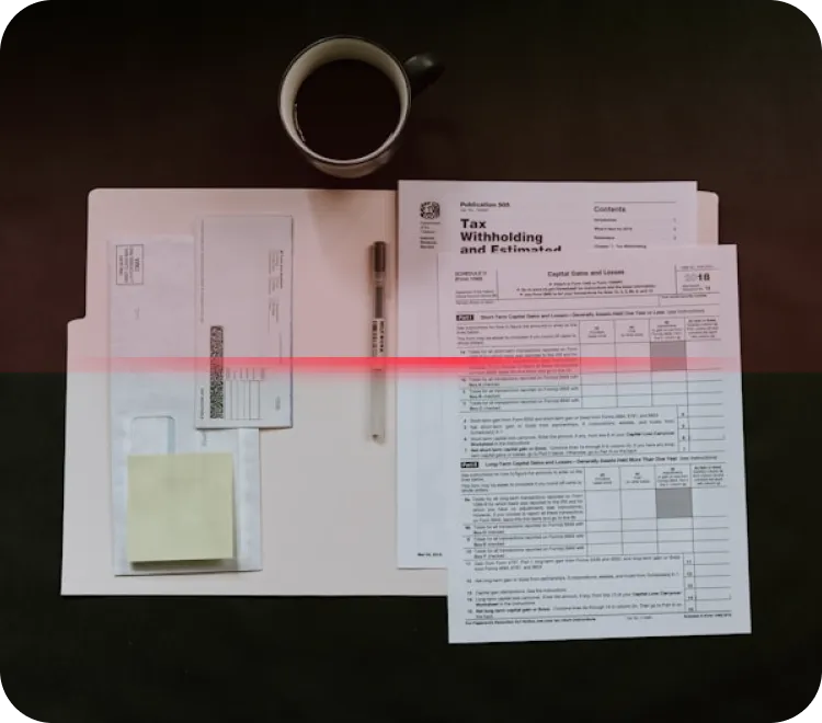 Top view of a coffee cup, pen, manila folder with envelopes and sticky notes, and IRS tax forms on a dark surface.