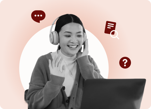 An Asian woman with headphones smiling and talking on her laptop.